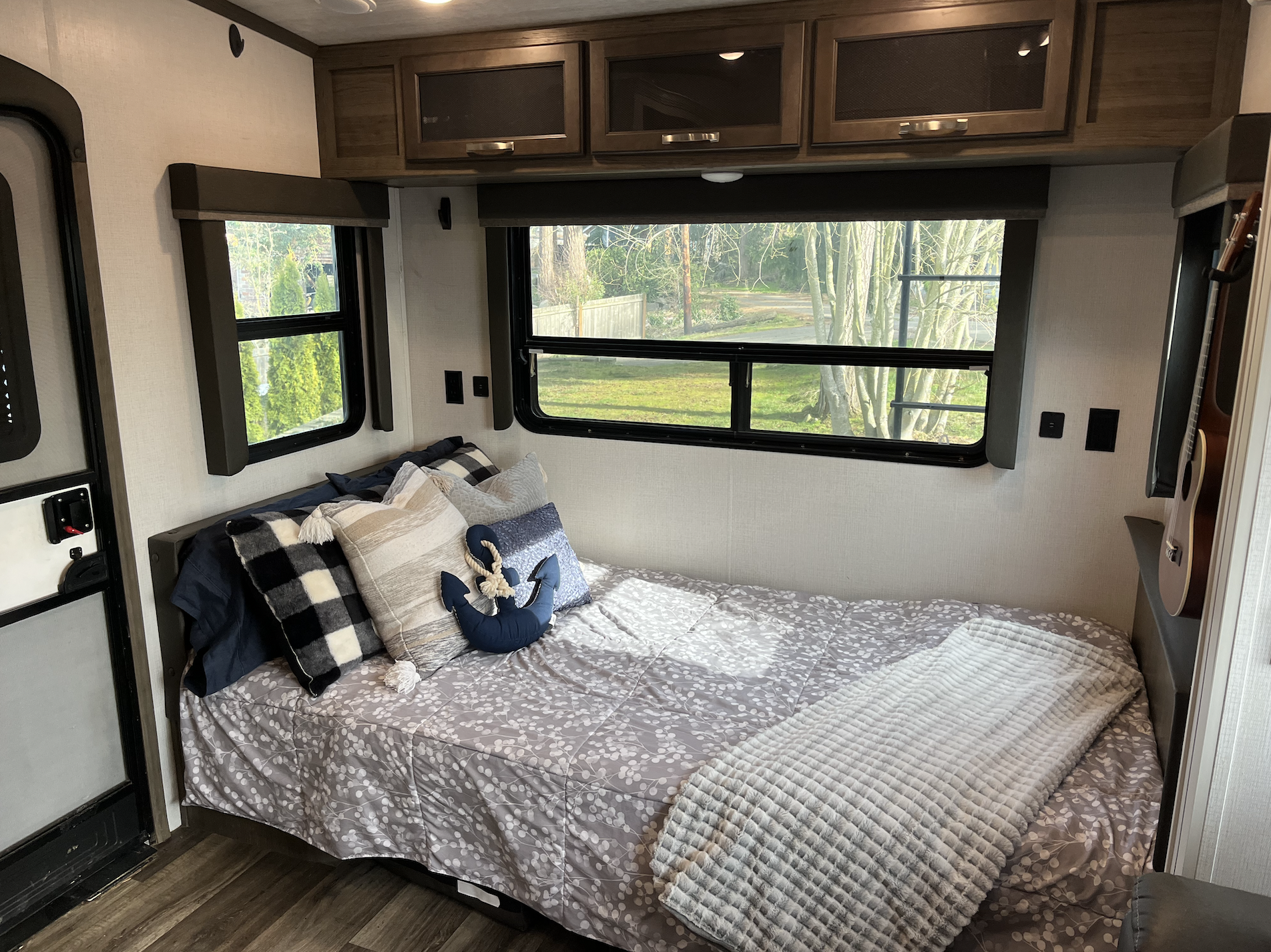 Cozy RV rental bedroom featuring a comfortable bed, blanket, pillows, cabinets, and windows with an outdoor view.. Keystone RV Cougar 2021