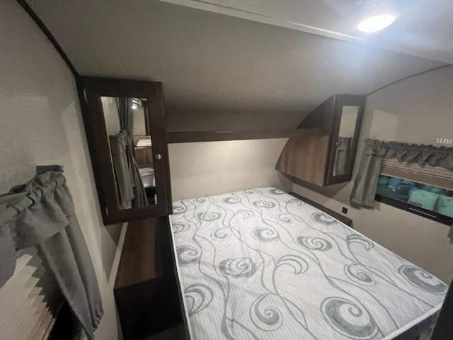 RV rental interior: A compact bedroom with a patterned bed, mirrored storage, and window with blinds.. Forest River Shasta Oasis 2018