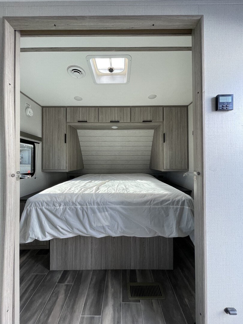 RV rental: Bright bedroom with a bed, wood-grain cabinets, and a ceiling skylight. Dark wood-look floor. Thermostat seen on the right.. Keystone RV Passport SL 2022