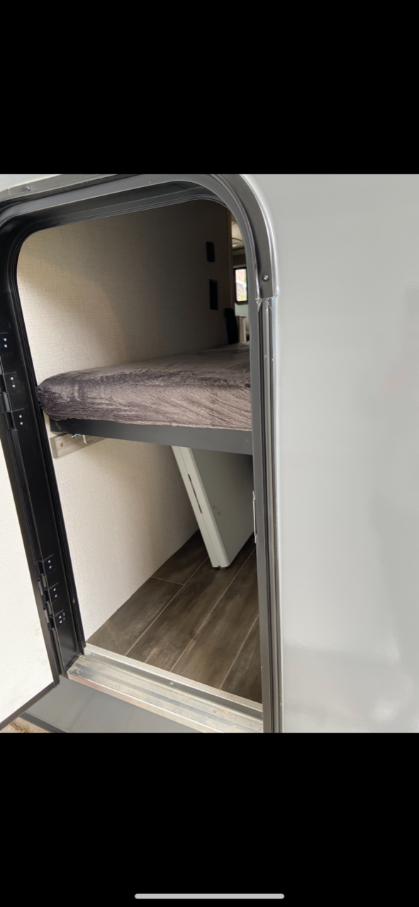 Peek inside an RV rental! Features a comfy bunk bed with a fuzzy blanket and wood flooring, seen through an open side hatch.. Keystone RV Passport SL 2022