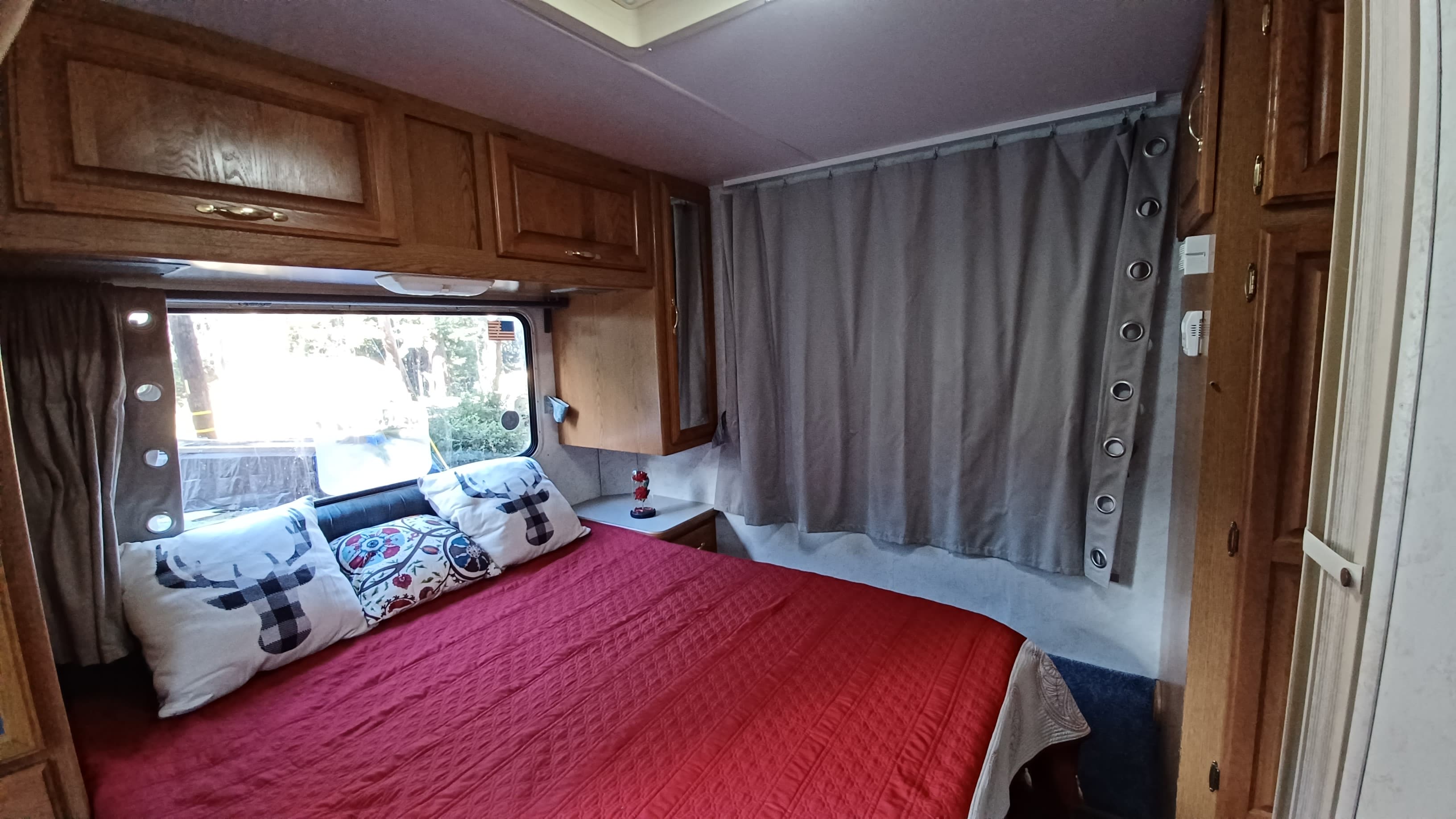 Cozy RV rental bedroom with a red bed, wooden cabinets, and window views. Perfect for your next RV adventure.. Four Winds 5000 2000