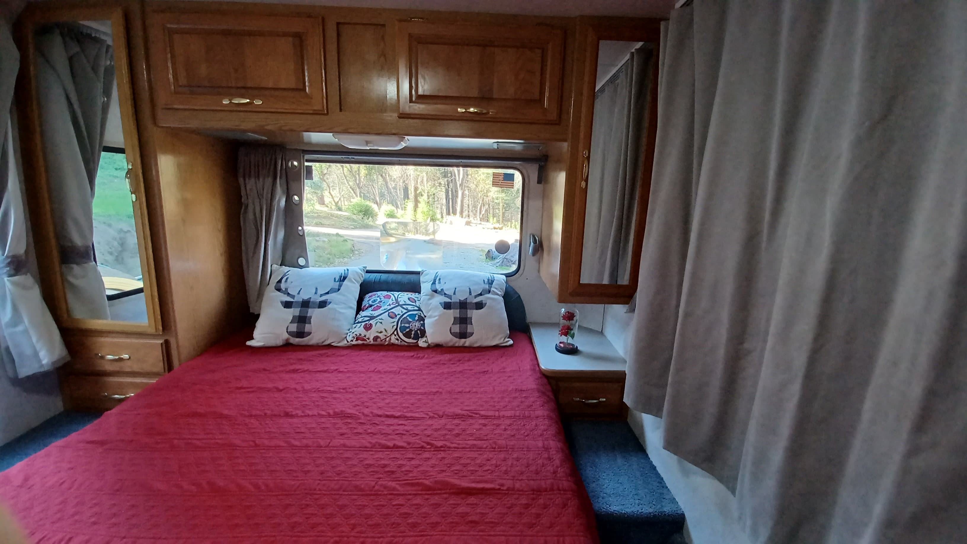 Comfortable RV rental bedroom: red bed, deer pillows, wood cabinets, and an outside wooded view for your travels.. Four Winds 5000 2000