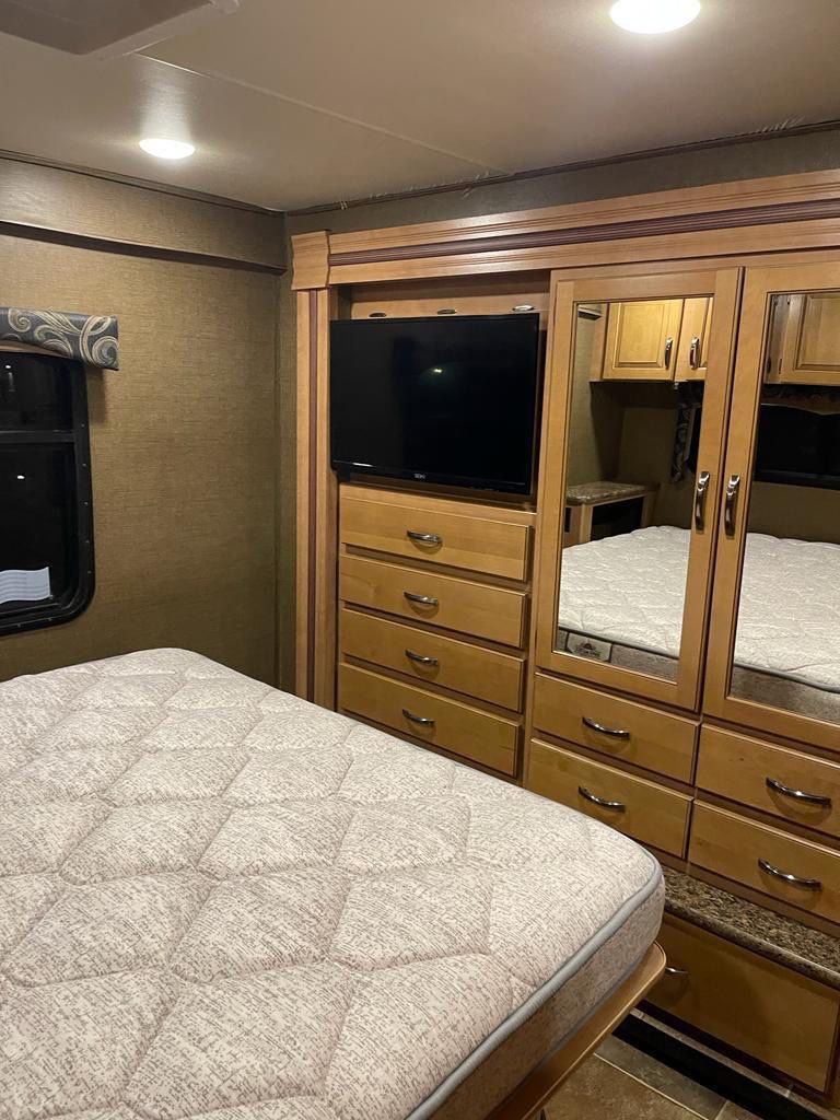 Comfortable RV rental bedroom featuring a large bed, built-in TV, and mirrored storage cabinets.. Thor Four Winds 2016