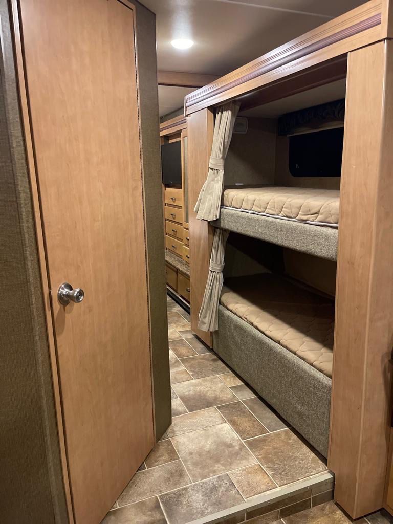 An RV rental's bedroom area with stacked bunk beds, privacy curtains, and durable tiled flooring.. Thor Four Winds 2016