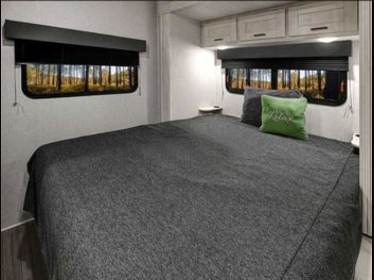 Comfortable RV rental bedroom with a large bed, forest views from the windows, and convenient overhead storage.. East to West 1FDWE3FN6NDC42920 2023