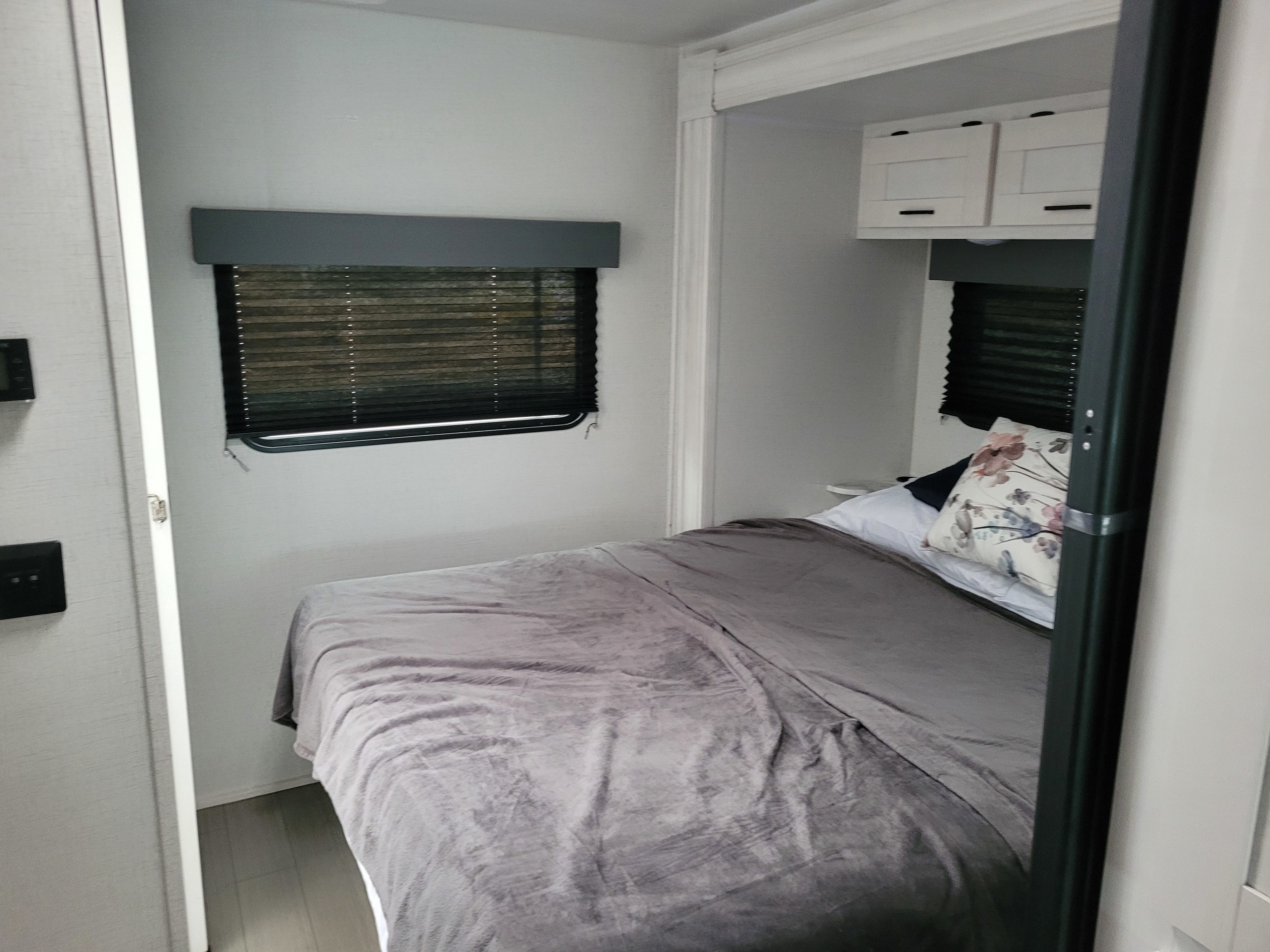 Cozy, modern RV rental bedroom with a comfortable bed, overhead cabinets, and dual windows. Perfect for your next adventure!. East to West 1FDWE3FN6NDC42920 2023