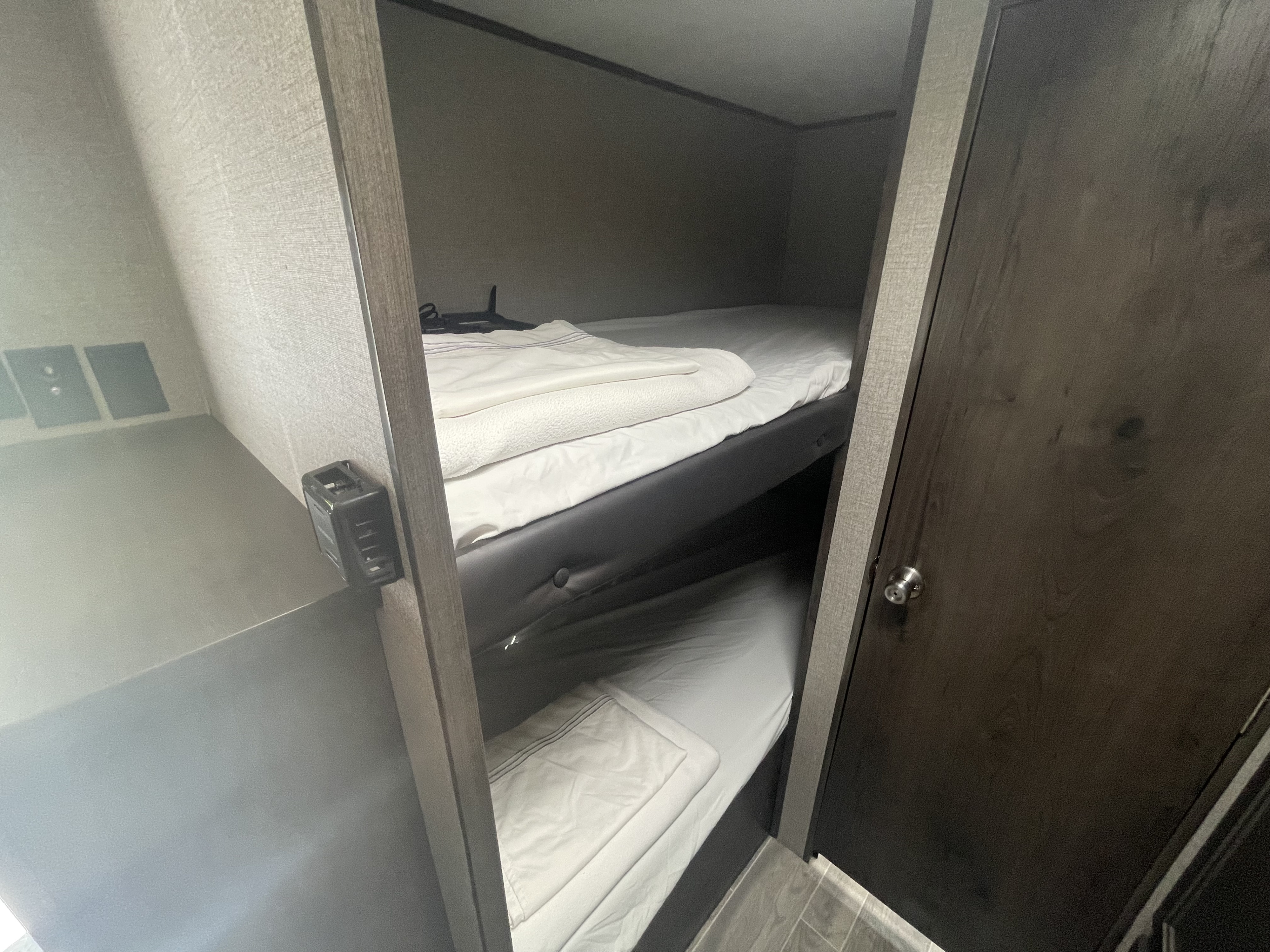 View inside an rv rental, showing compact bunk beds with white bedding, wall outlets, and a control panel.. Jayco Jay Flight 2021