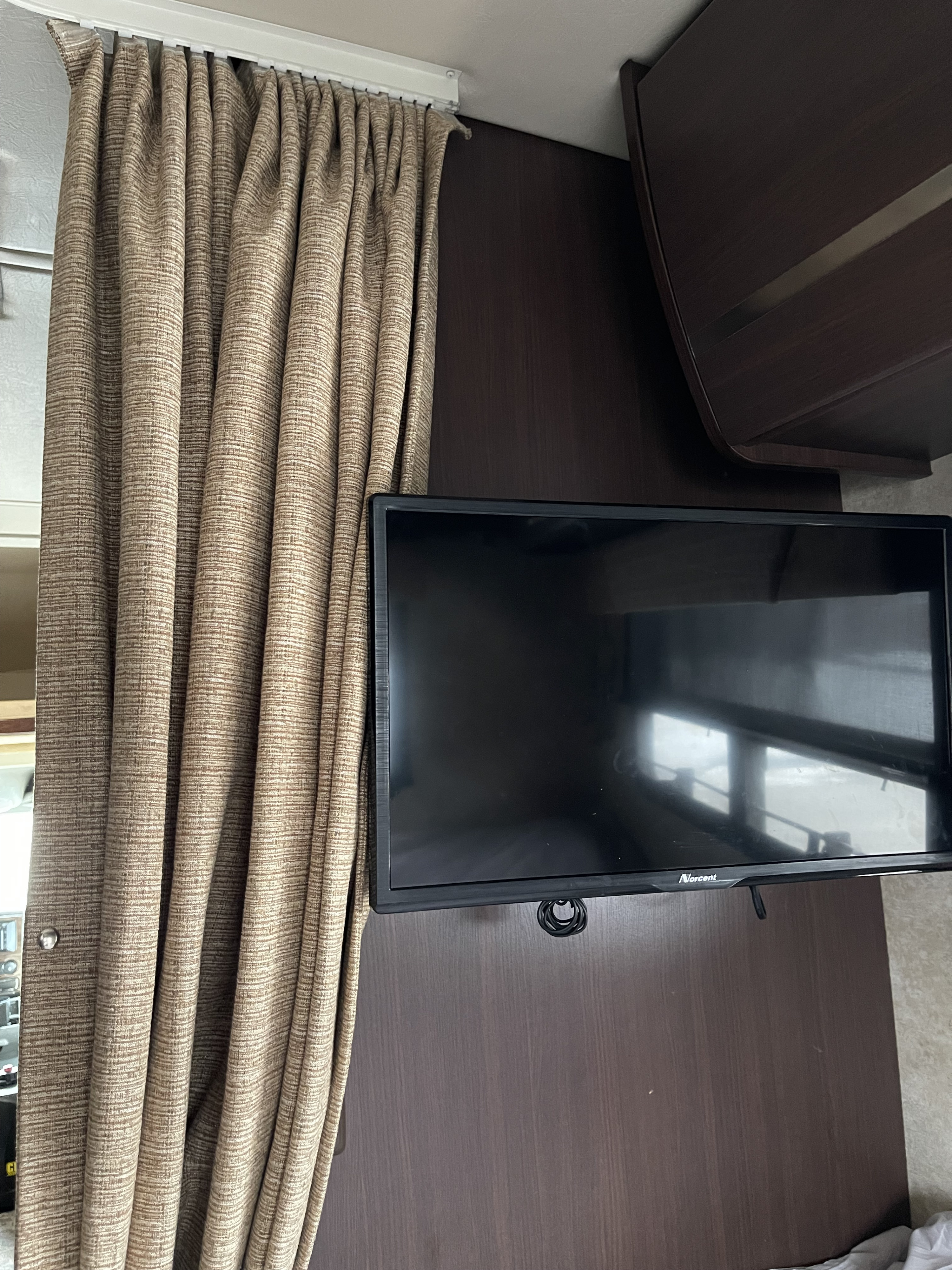 RV rental interior showing textured tan curtains, wall-mounted TV, and dark wood paneling. A compact living space.. Winnebago View 2011