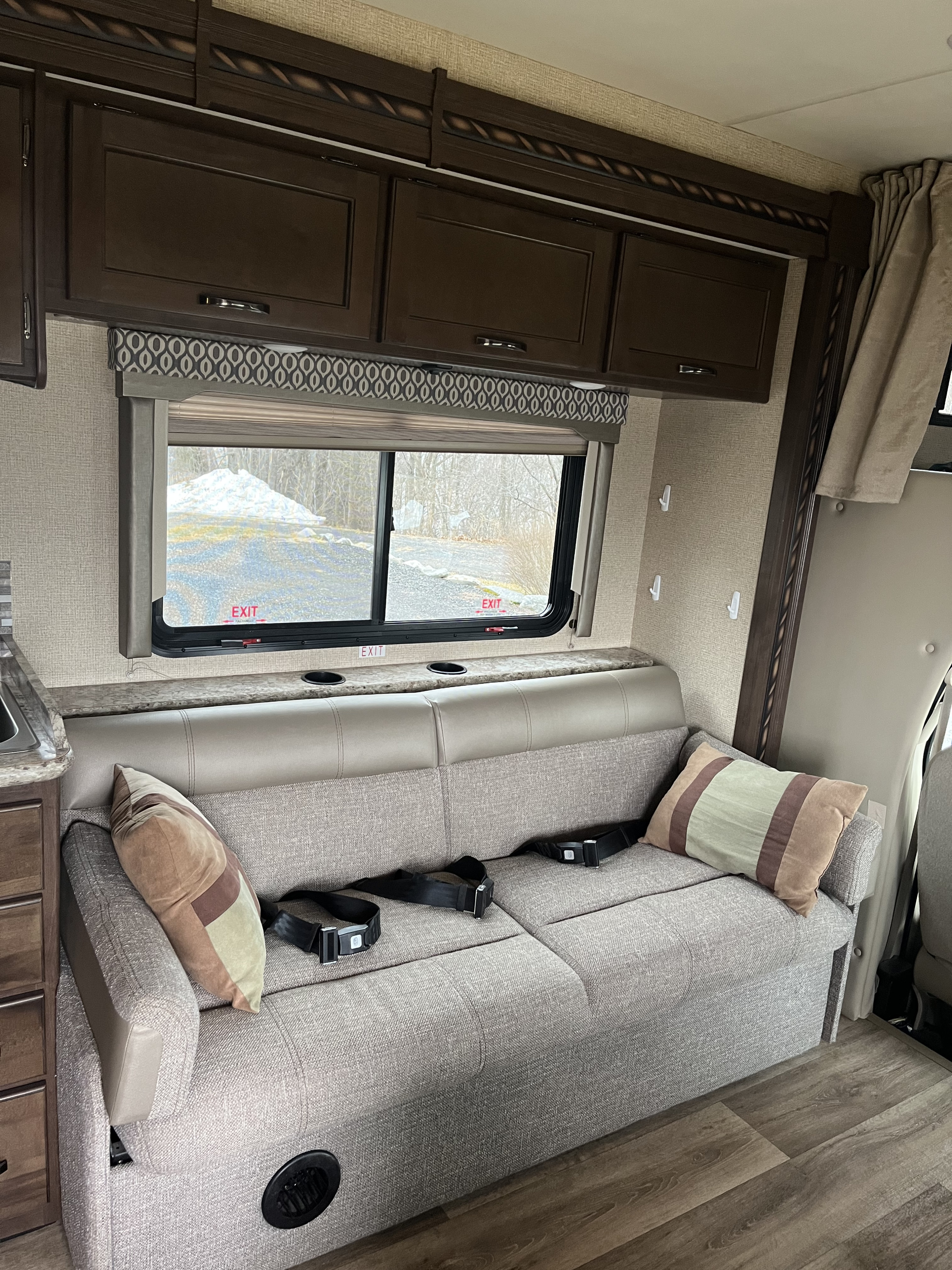 RV rental interior: A cozy dinette sofa with seatbelts, overhead cabinets, and a scenic window view.. Thor Freedom Elite 2017