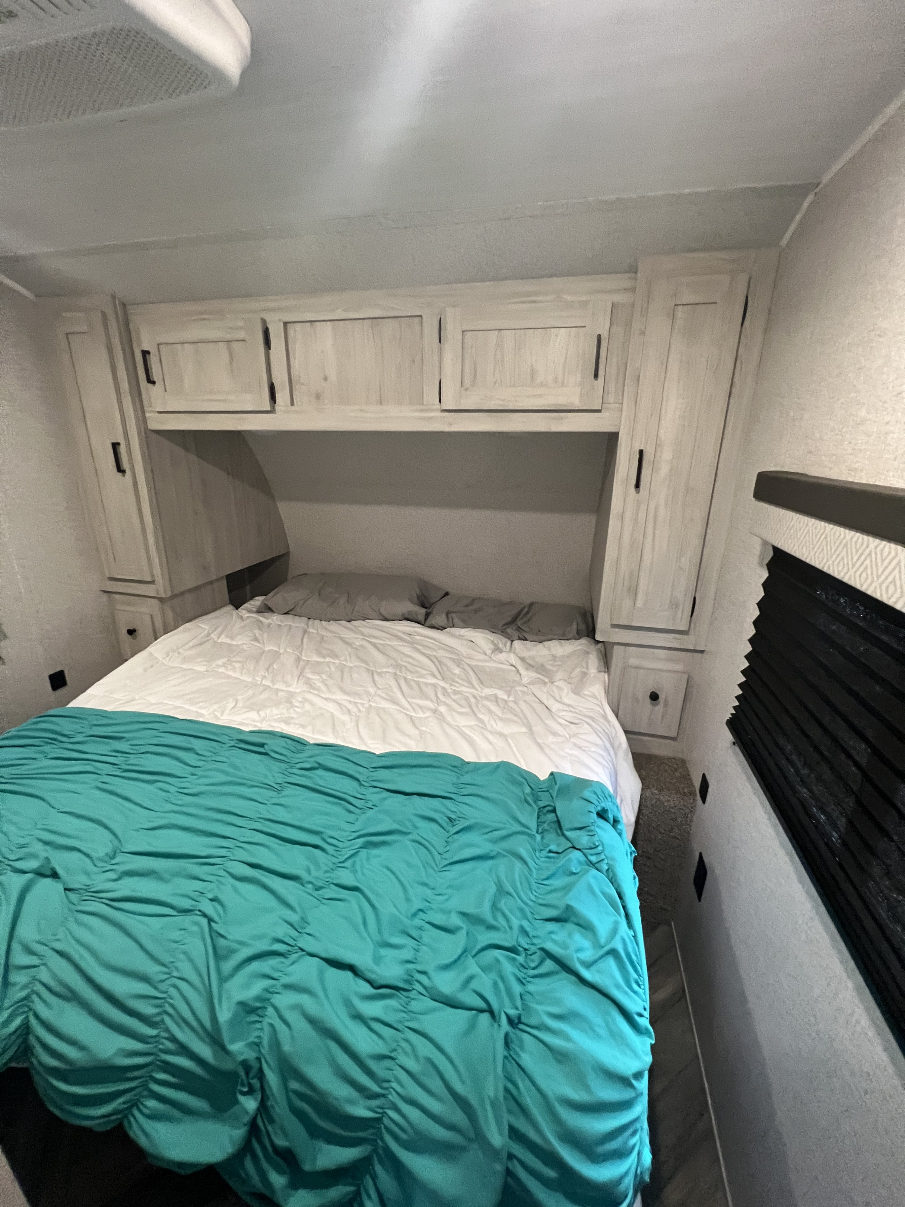 View inside an RV rental bedroom showing a bed with teal & white bedding, overhead cabinets, and an AC vent.. East to West Della Terra 2022