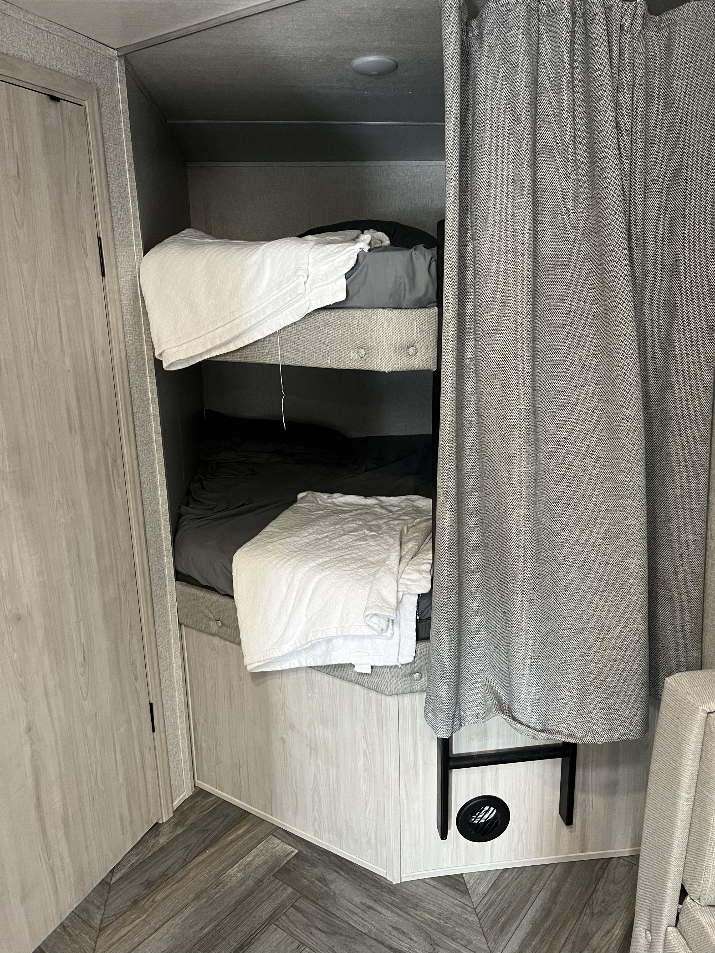 RV rental bunk beds in a light wood interior. Includes comfy bedding, privacy curtain, and access ladder.. East to West Della Terra 2022
