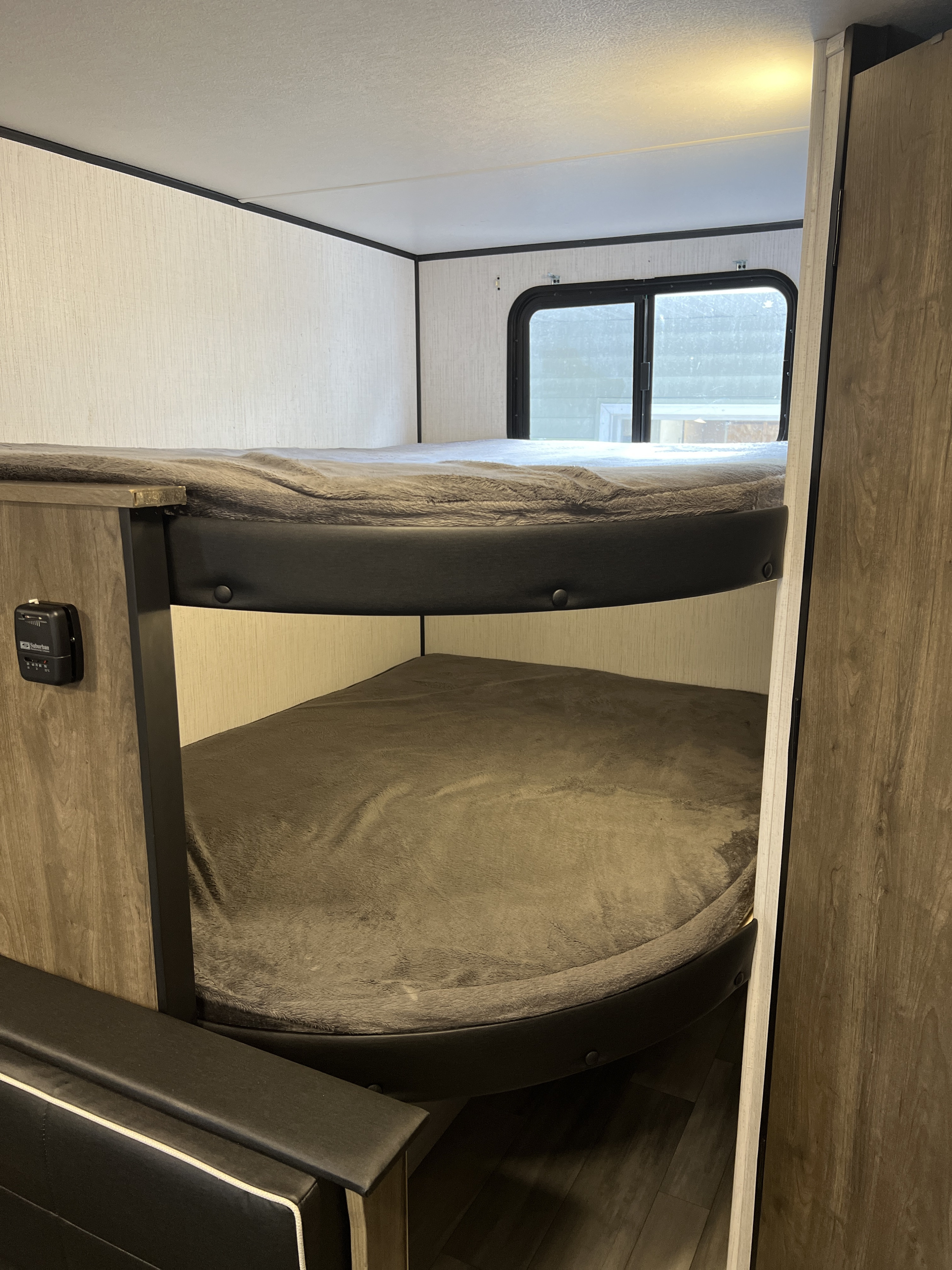 Cozy RV rental interior featuring comfortable bunk beds with gray blankets, a window, and wood-look accents.. Heartland RVs Pioneer Trail Blazer 2022