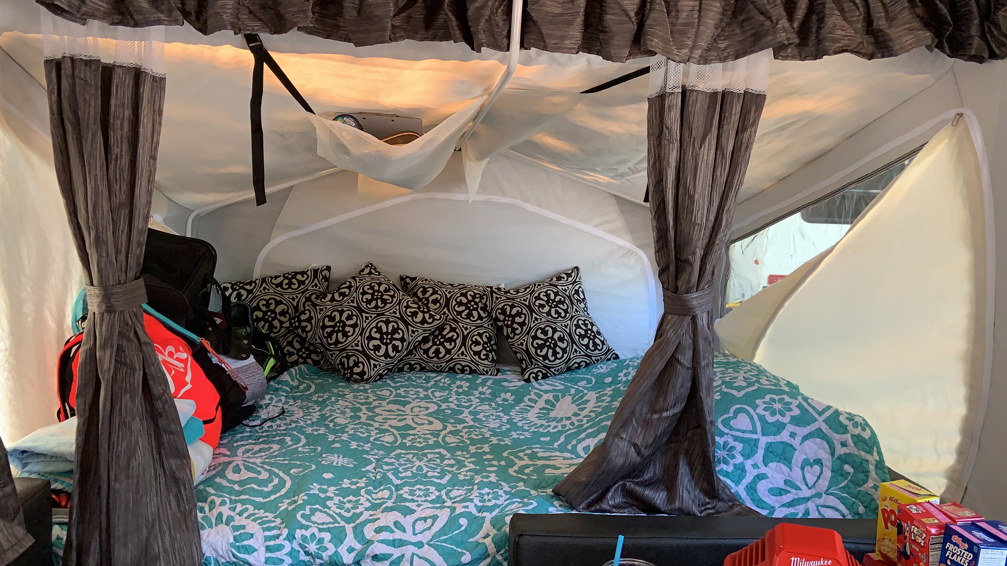 RV rental interior shows a cozy bed with turquoise quilt, patterned pillows, luggage, & snacks. Great for campers.. Forest River Palomino Compass 2017