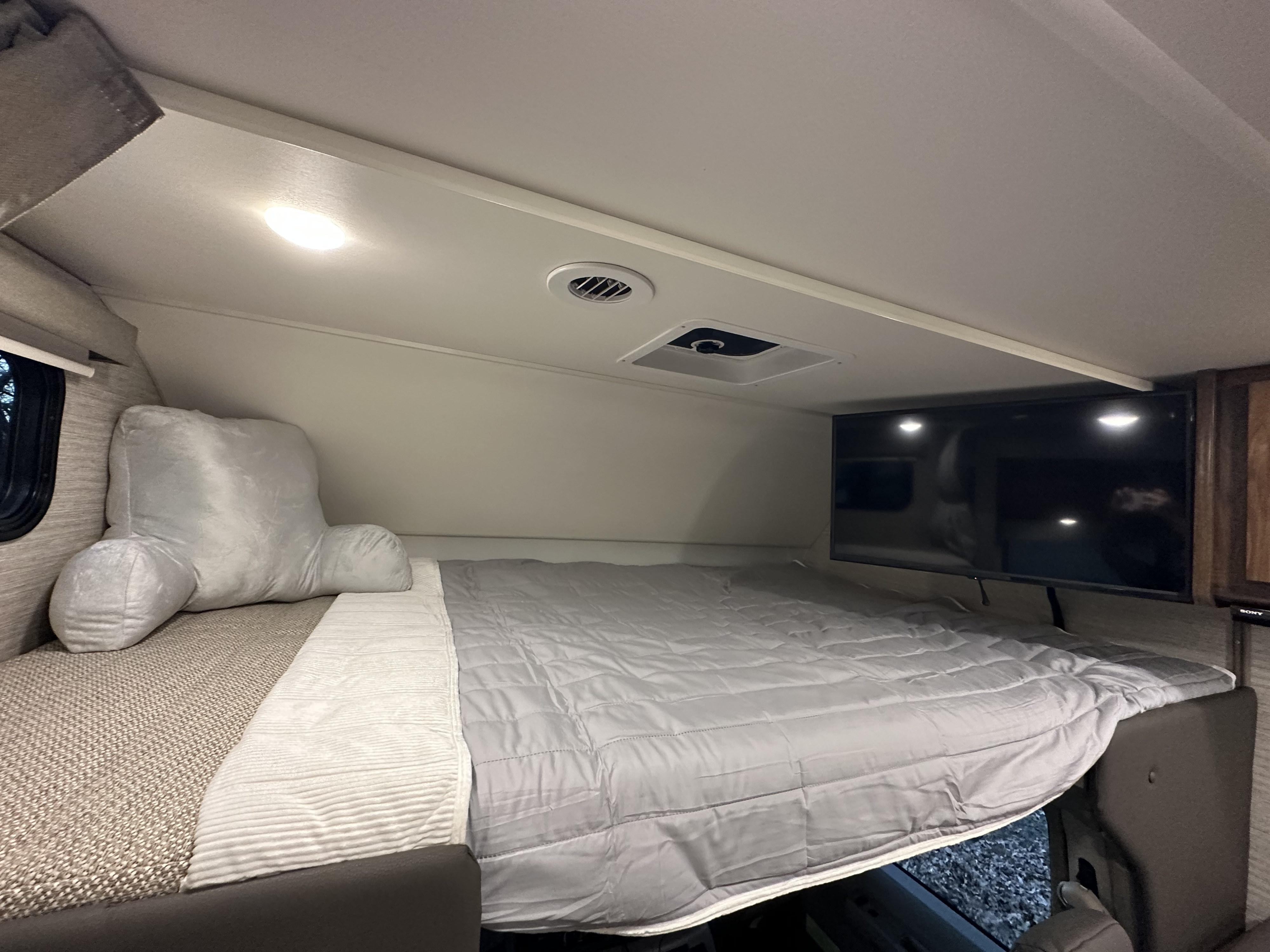 RV rental interior: A comfortable bed with a grey comforter, large pillow, and wall-mounted TV, ideal for relaxing.. Winnebago Minnie Winnie 2021