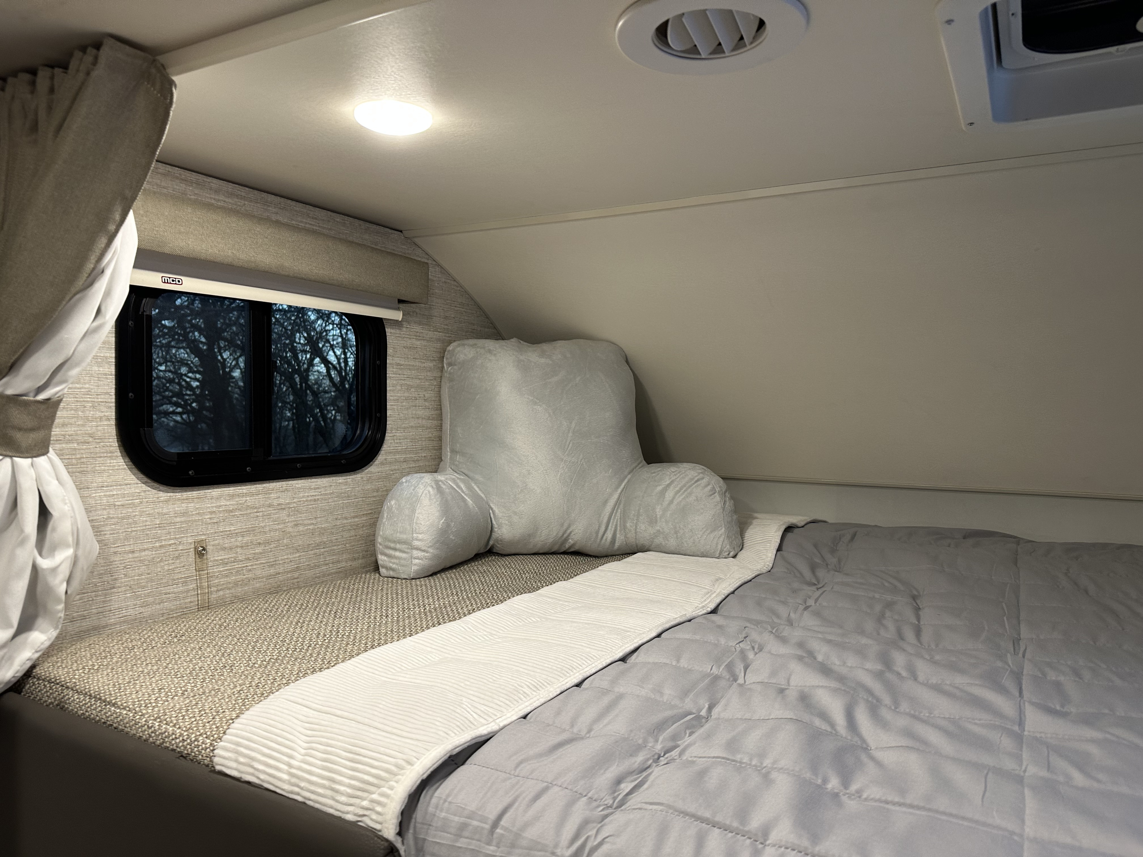 RV rental's cozy bedroom: a comfy bed with grey comforter, reading pillow, window, and ceiling light.. Winnebago Minnie Winnie 2021
