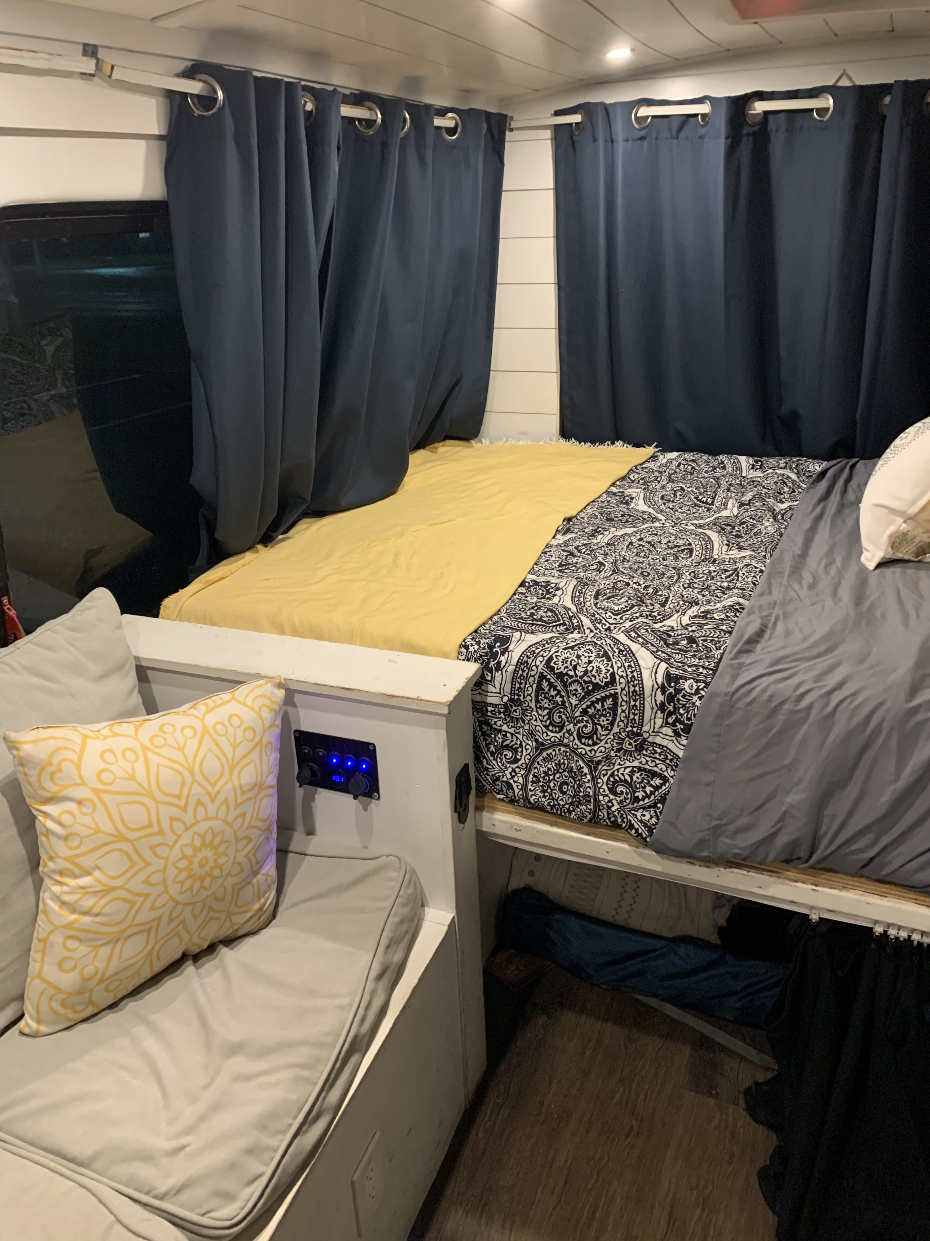 Cozy RV rental interior featuring a versatile bed/lounge area, dark privacy curtains, and convenient power outlets.. Ford Real Lite Econoline 350 2014