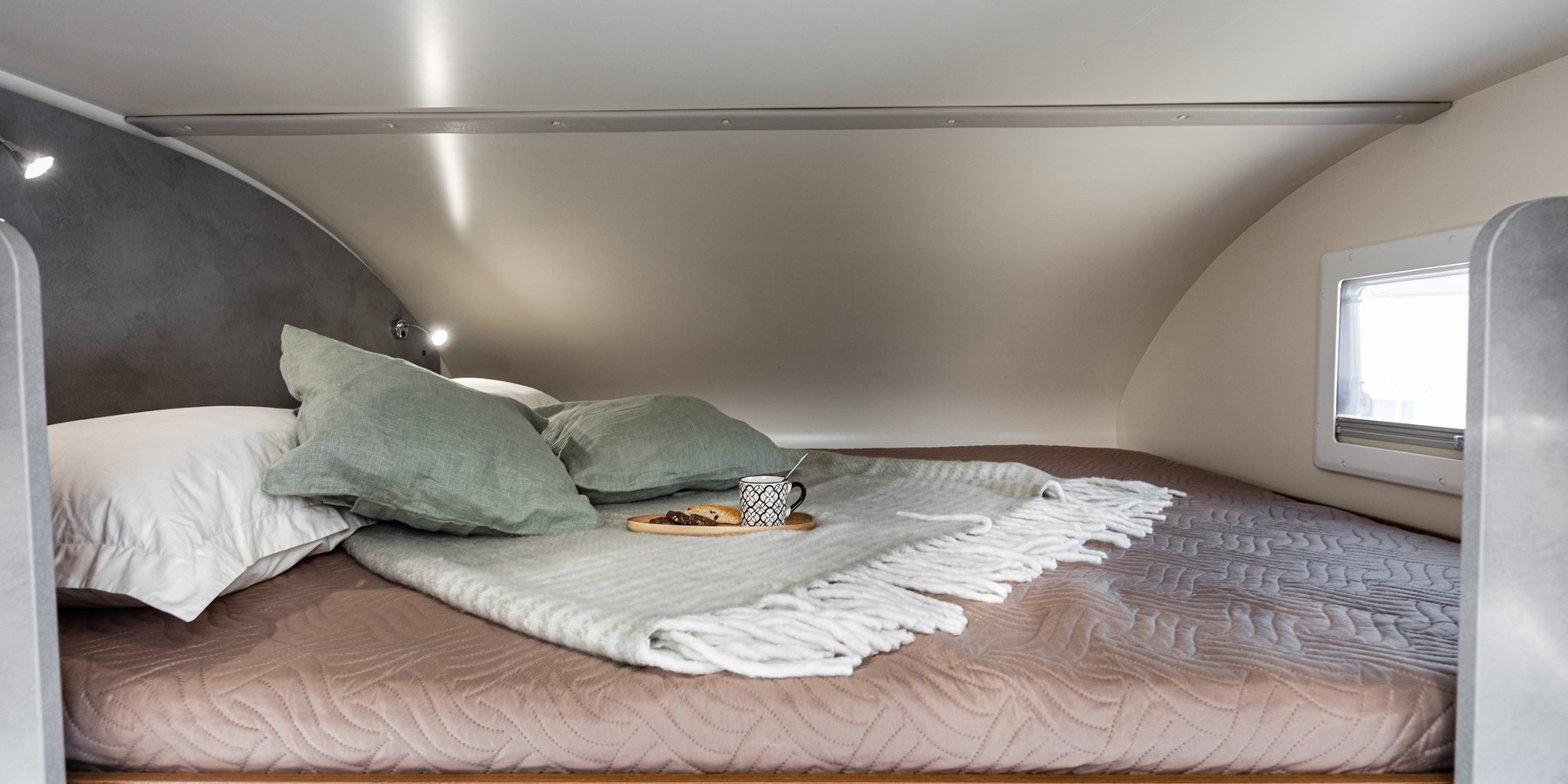 RV rental bedroom showing a cozy bed with green pillows, a blanket, and a tray of coffee and snacks.. Elnagh Baron 65 2023