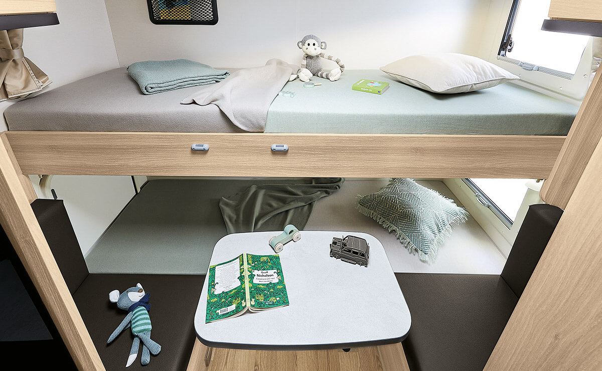 RV rental interior with cozy bunk beds. Upper bunk has bedding & toys; lower converts to a dinette with table, seats, & play area.. Itineo CS660 2023