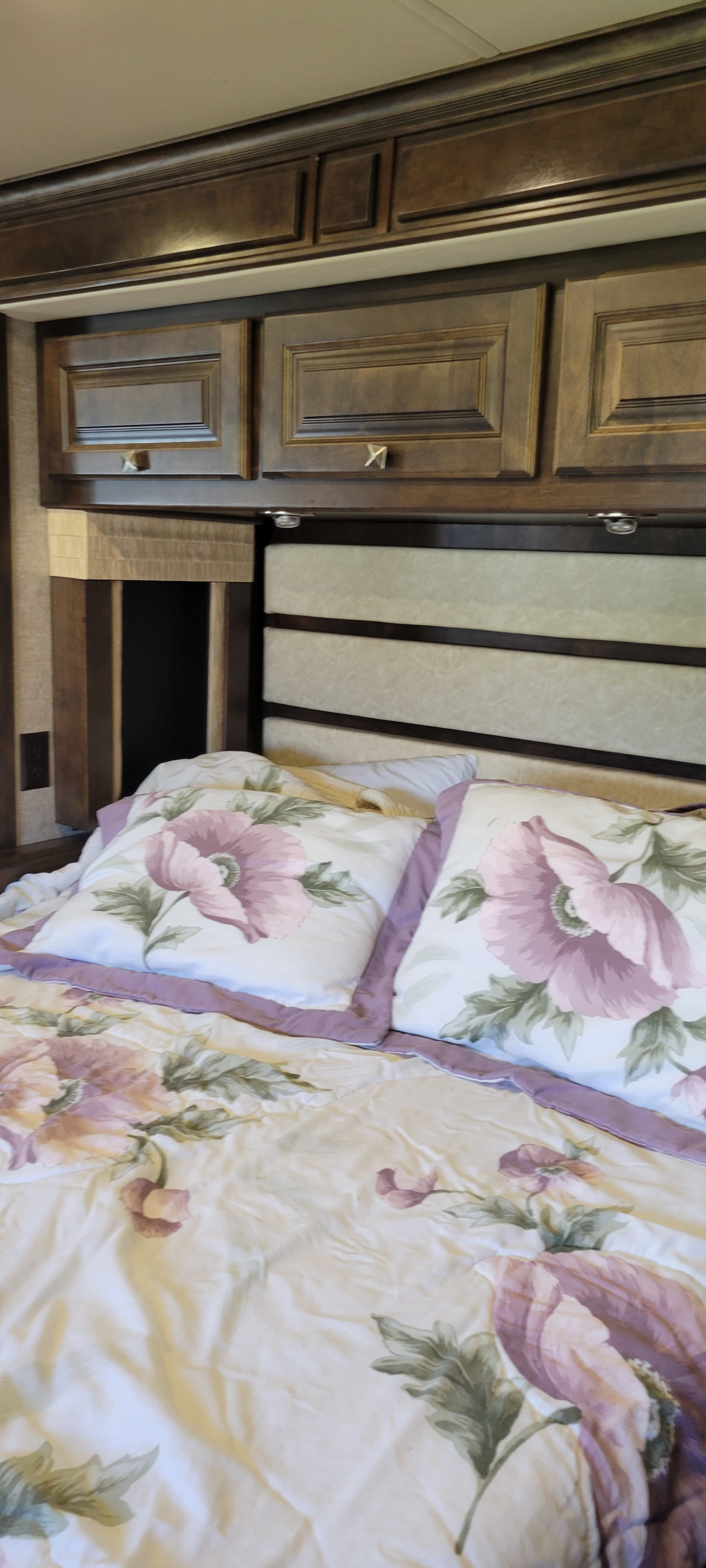 Cozy RV rental bedroom featuring floral bedding, upholstered headboard, and practical overhead wood cabinets.. Breeze Breeze Motorhome 2017