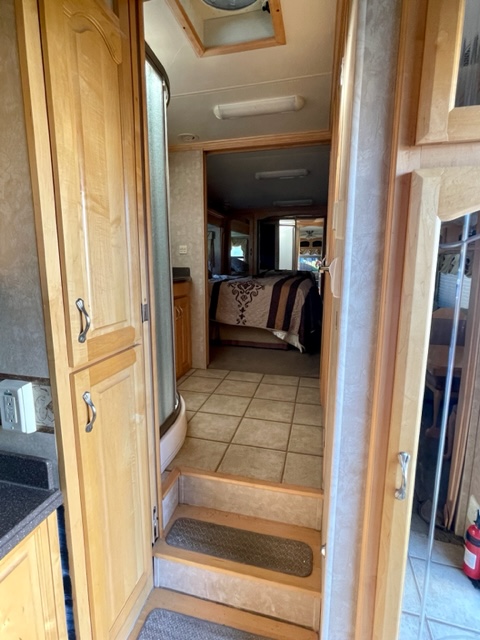 RV rental interior featuring a bedroom, steps to a tiled floor, and a shower/kitchenette area with wood cabinetry.. Escalade Escalade Fifth Wheel 2007