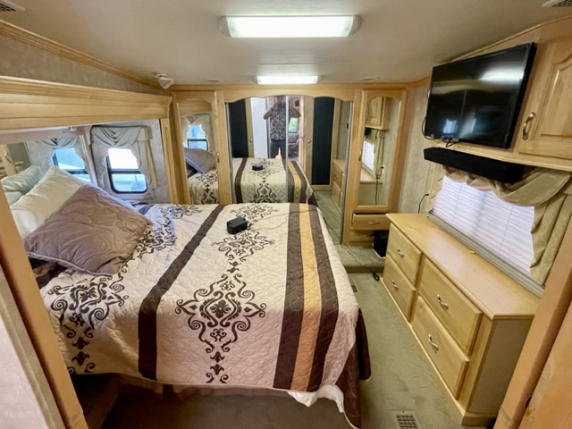 RV rental bedroom with patterned bed, dresser, TV, and mirrored closet. A person is visible in reflection.. Escalade Escalade Fifth Wheel 2007