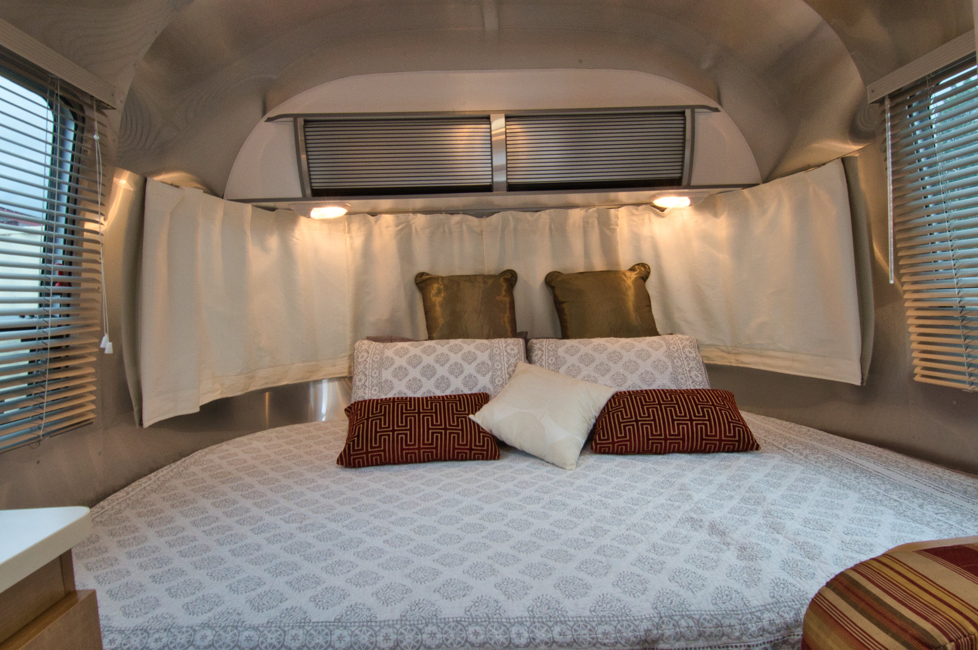 Experience comfort in this RV rental's cozy Airstream bedroom, featuring a plush bed, patterned pillows, and warm lighting.. Airstream Sport 2012