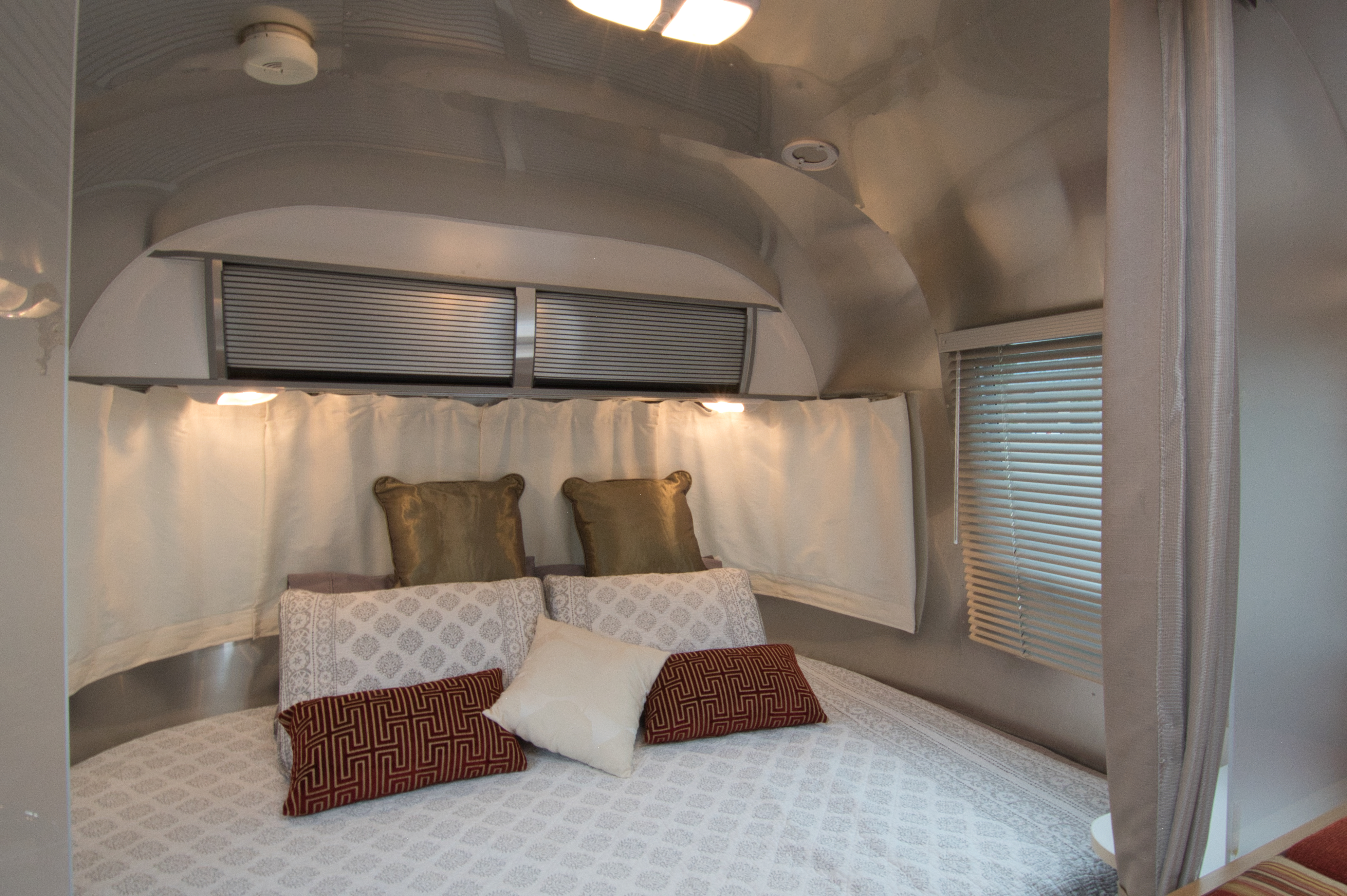 Cozy RV rental bedroom featuring a comfortable bed with patterned pillows, blinds, and interior lighting.. Airstream Sport 2012