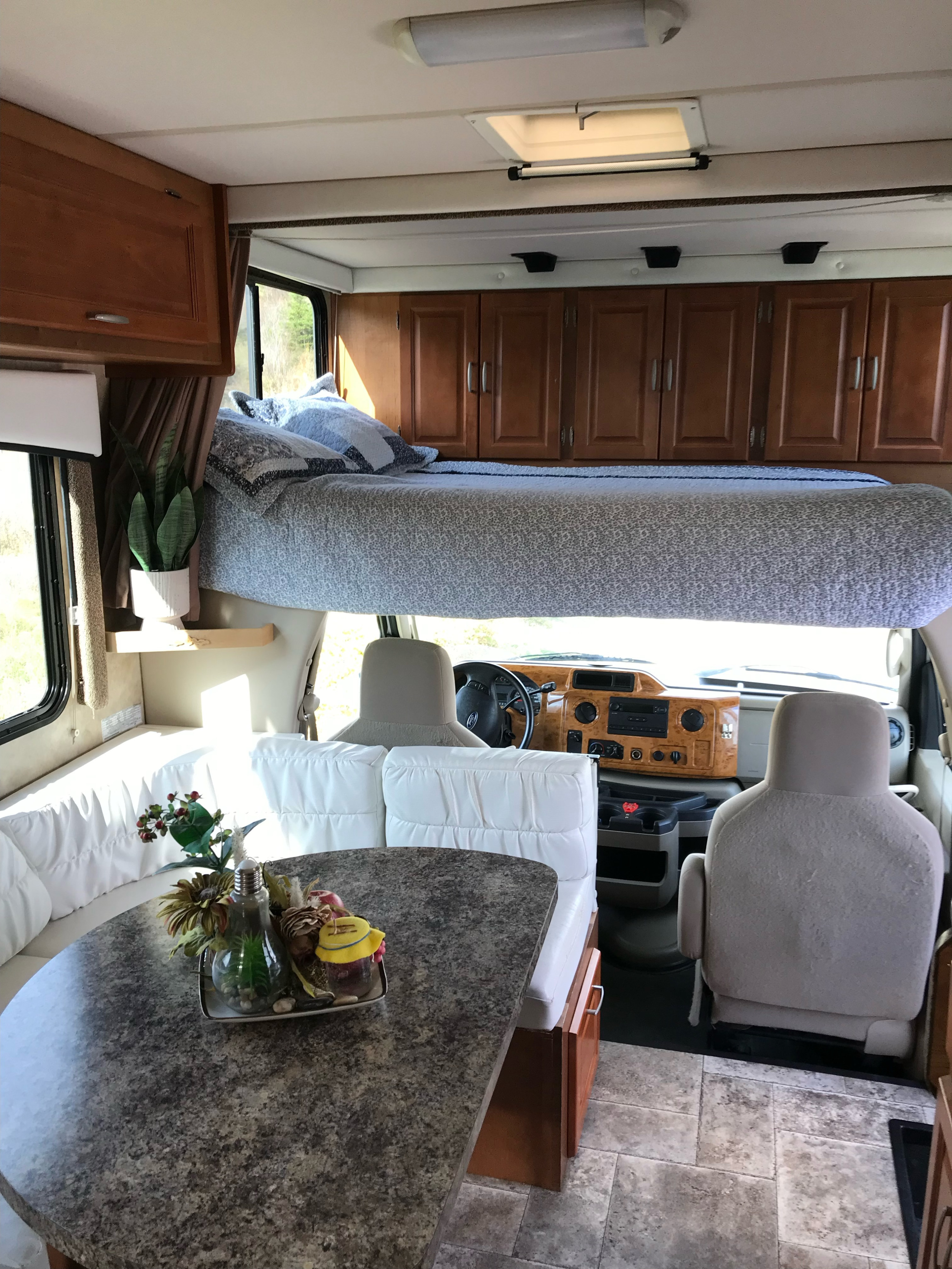 View of a clean and spacious RV rental interior, showcasing the over-cab bed, dinette, and driver's area.. Ford CTV 2011
