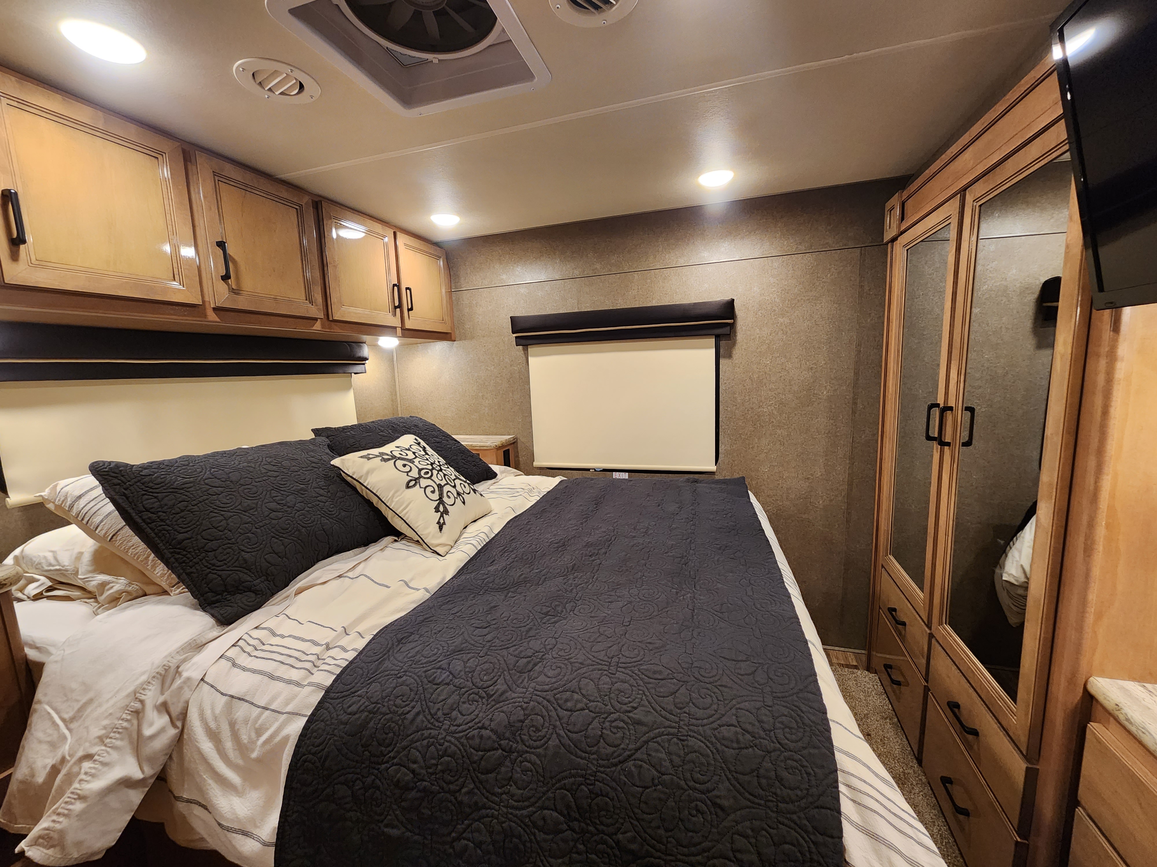 Cozy RV rental bedroom with dark bedding, overhead cabinets, and mirrored closet. Ideal for comfortable travel.. Thor Motor Coach Quantum 2019