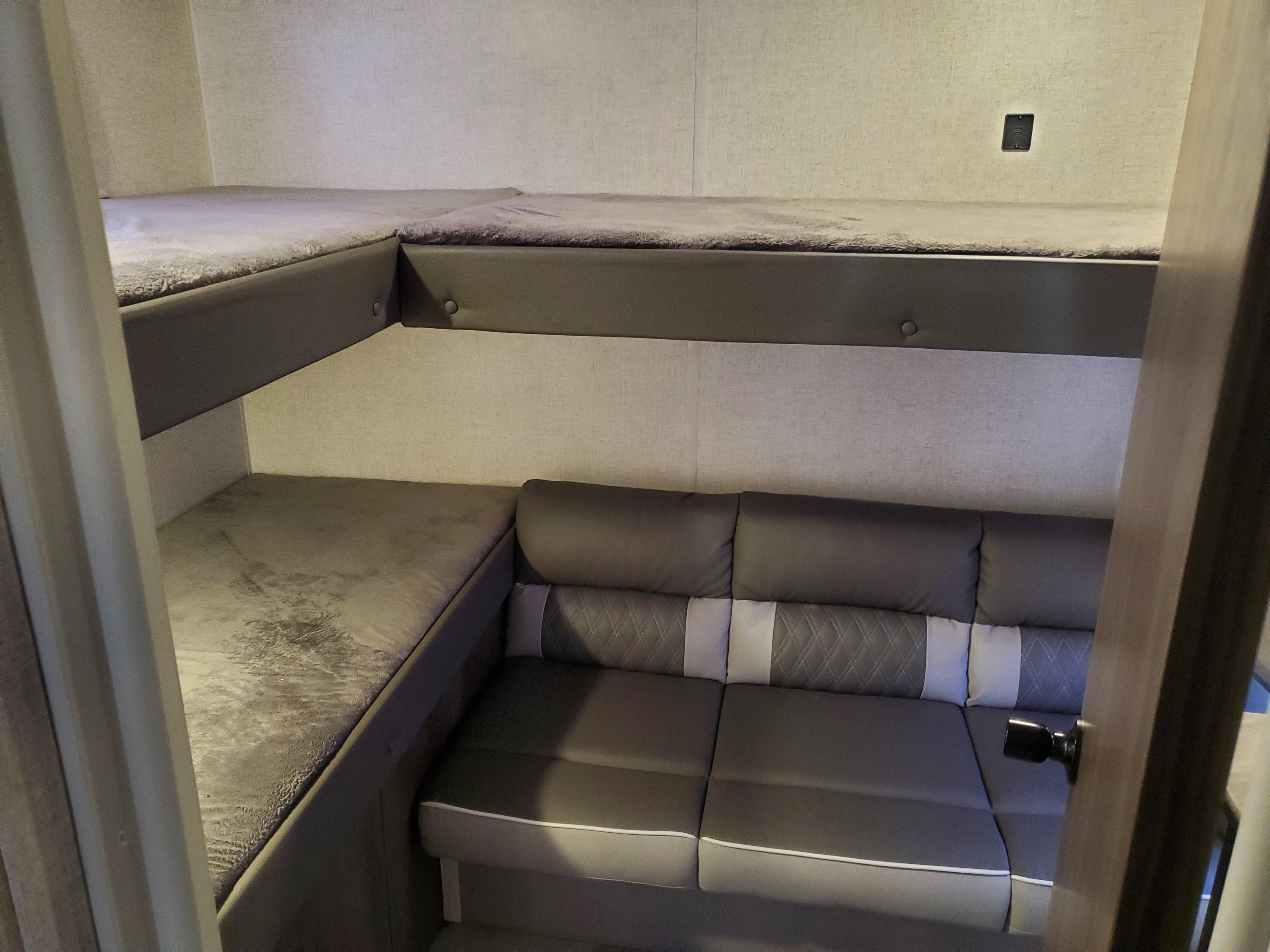 Interior of an **rv rental** showing stacked bunk beds and a comfortable sofa with patterned cushions and white trim.. Forest River Wildwood X-Lite 2021