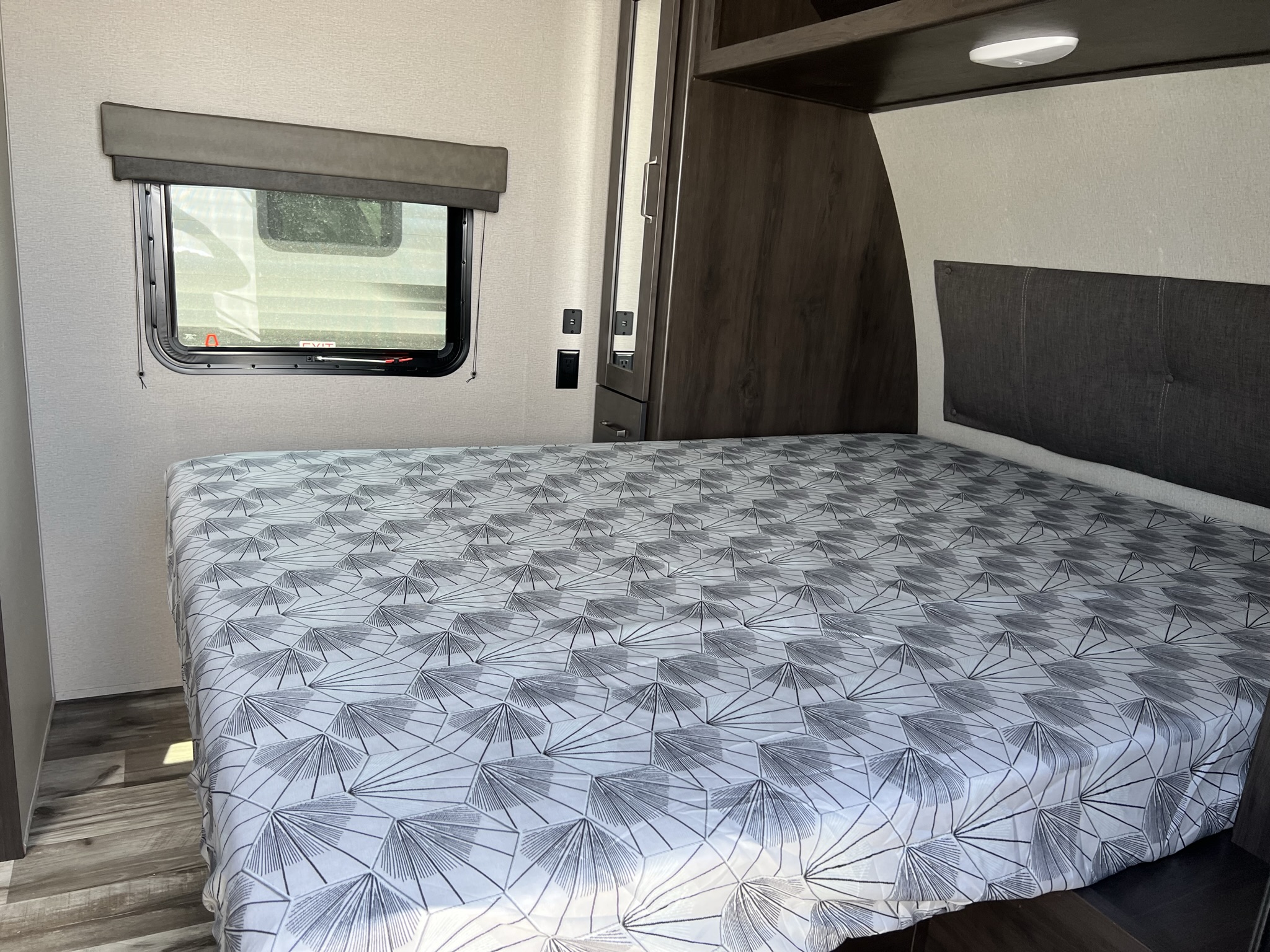 Interior of an RV rental bedroom showing a bed with geometric sheet, window, wardrobe, and USB charging outlets.. Grand Design Transcend Xplor 2022