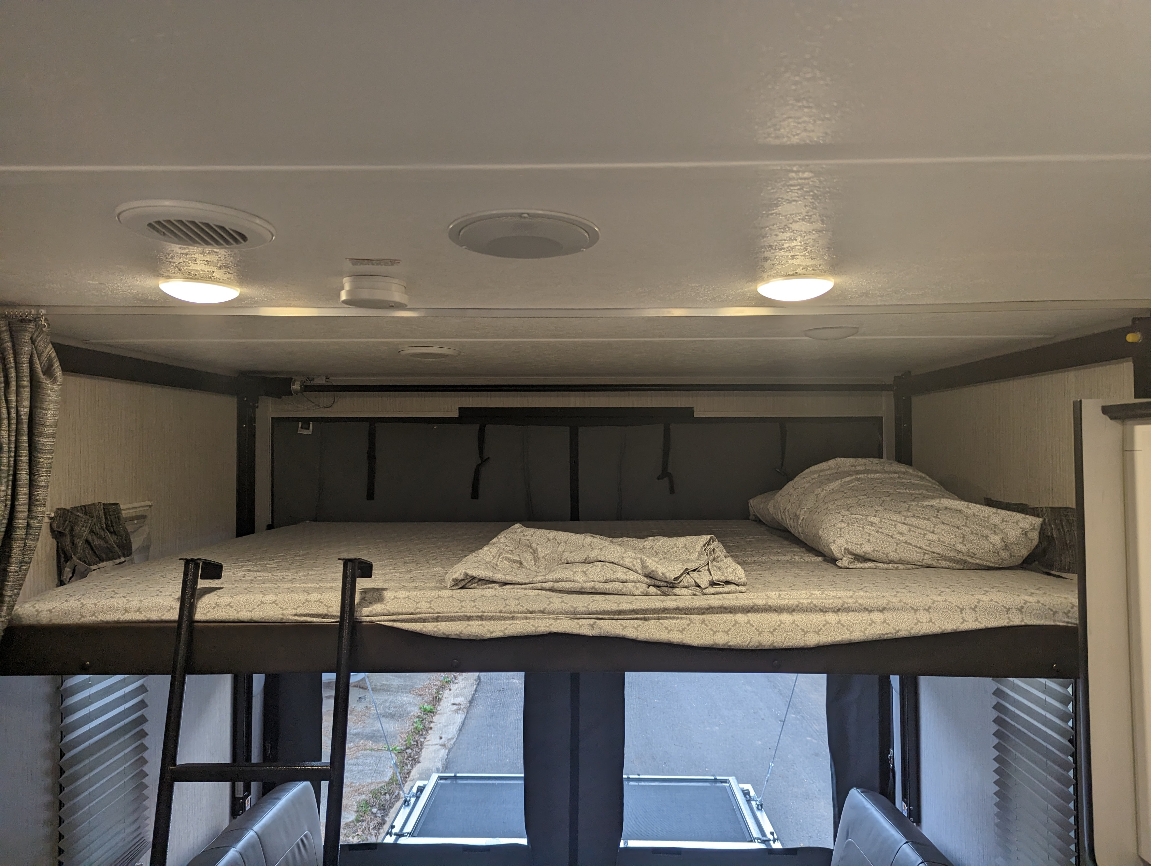 An RV rental's elevated bed with a ladder, patterned bedding, and ceiling features like lights and vents.. Forest River Puma 2022
