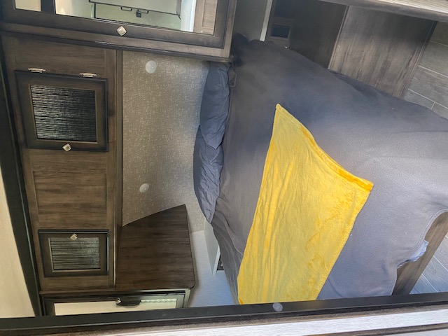 RV rental bedroom: Cozy interior with dark wood cabinets, a comfortable bed, and a bright yellow blanket.. Heartland RVs Wilderness 2020