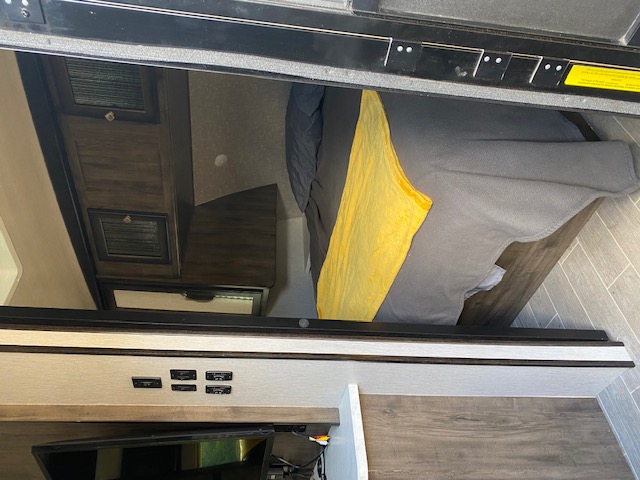 RV rental interior: A cozy bedroom with a bed, wood cabinets, and entertainment console. Modern camper amenities.. Heartland RVs Wilderness 2020