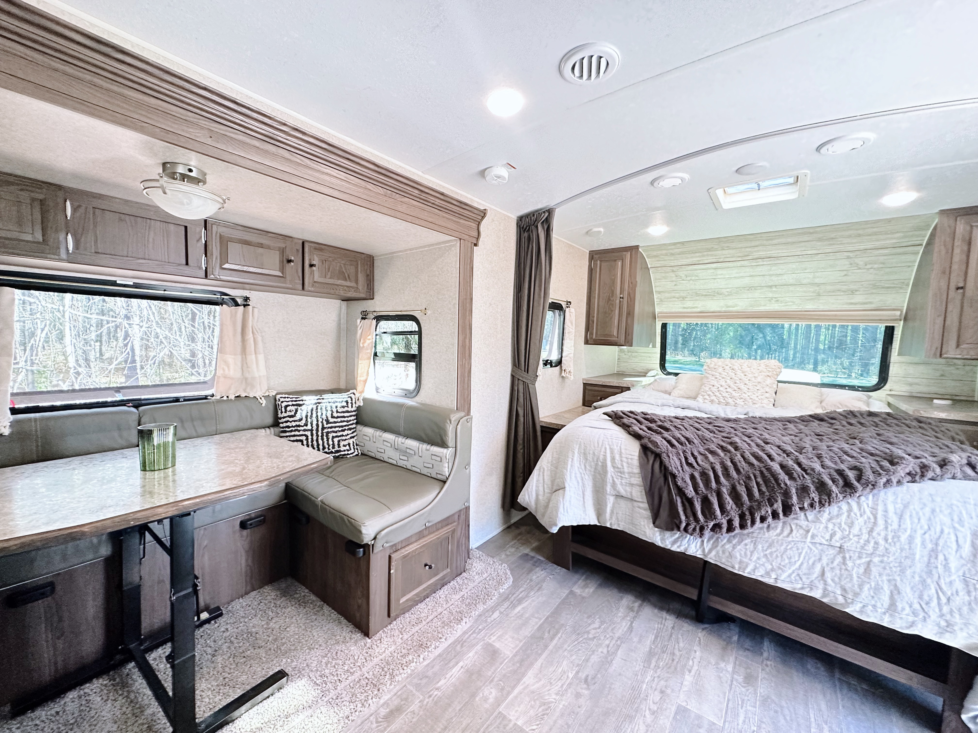An inviting RV rental interior featuring a bright bedroom area with a comfy bed and a dining booth with a table.. Forest River Flagstaff Micro Lite 2019