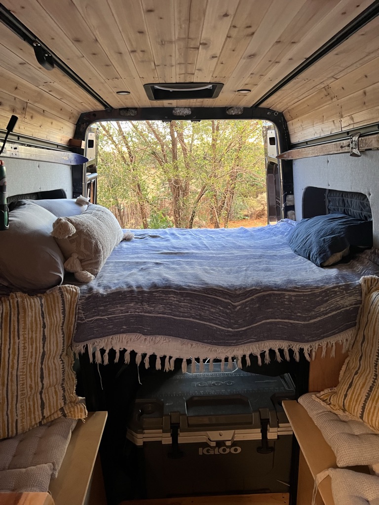 Cozy RV rental interior with bed, nature view out the back, and an Igloo cooler stored underneath.. Mercedes Sprinter Van 4x4 2020