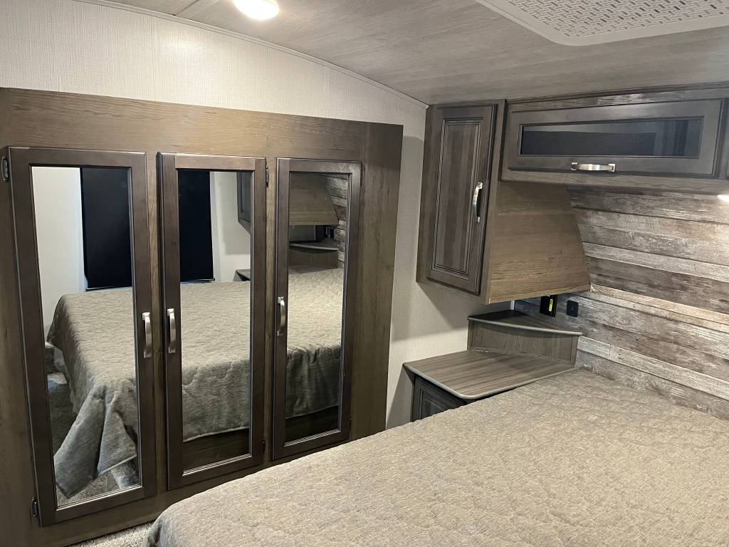 Cozy RV rental bedroom featuring a comfortable bed, mirrored wardrobe, and built-in overhead storage for optimized travel space.. Keystone Cougar 2022