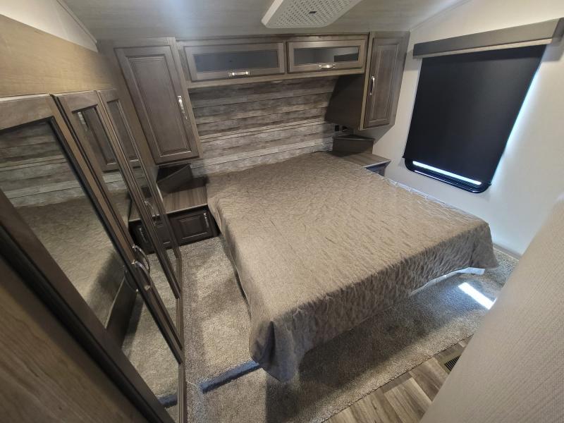 This RV rental bedroom features a bed, mirrored closet, overhead storage, and a window with a black shade.. Keystone Cougar 2022