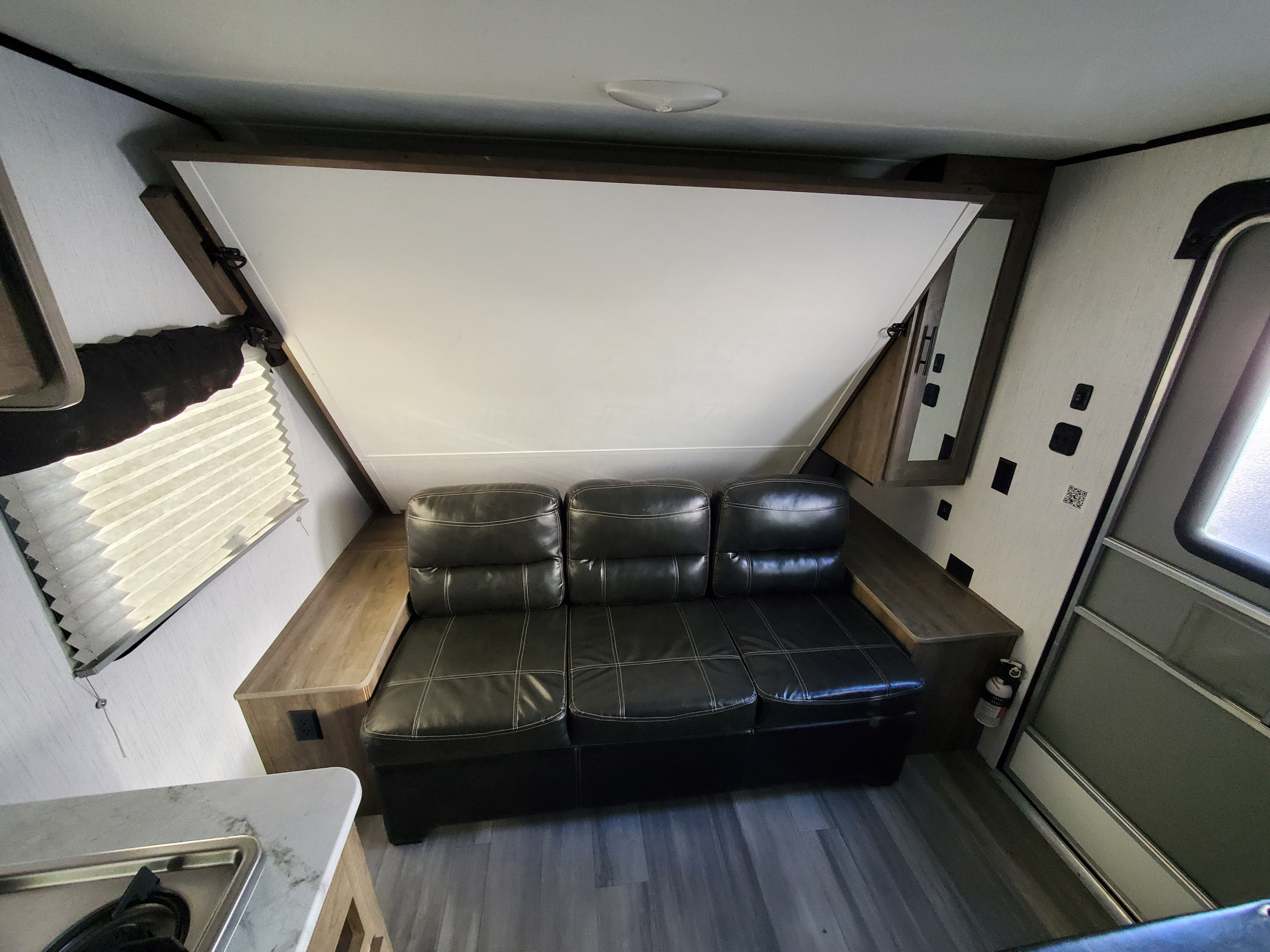 This RV rental interior features a black leather couch, a fold-down bed, and a compact kitchen area, optimizing space.. Heartland Pioneer 2021