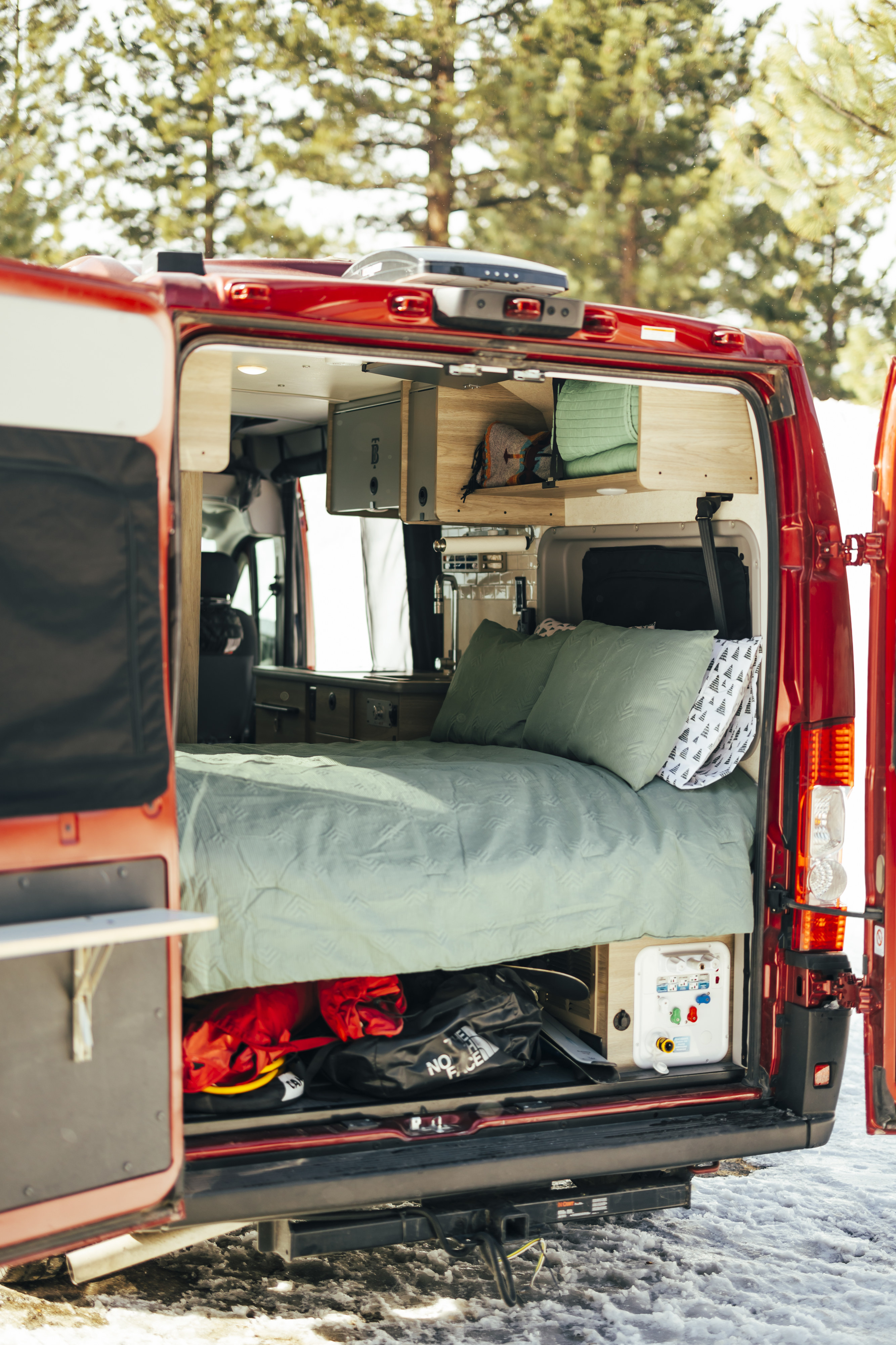 Inside this red RV rental camper van: a neatly made bed, overhead storage, and gear stowed below, ready for adventure.. Solis 59P Solis 2022