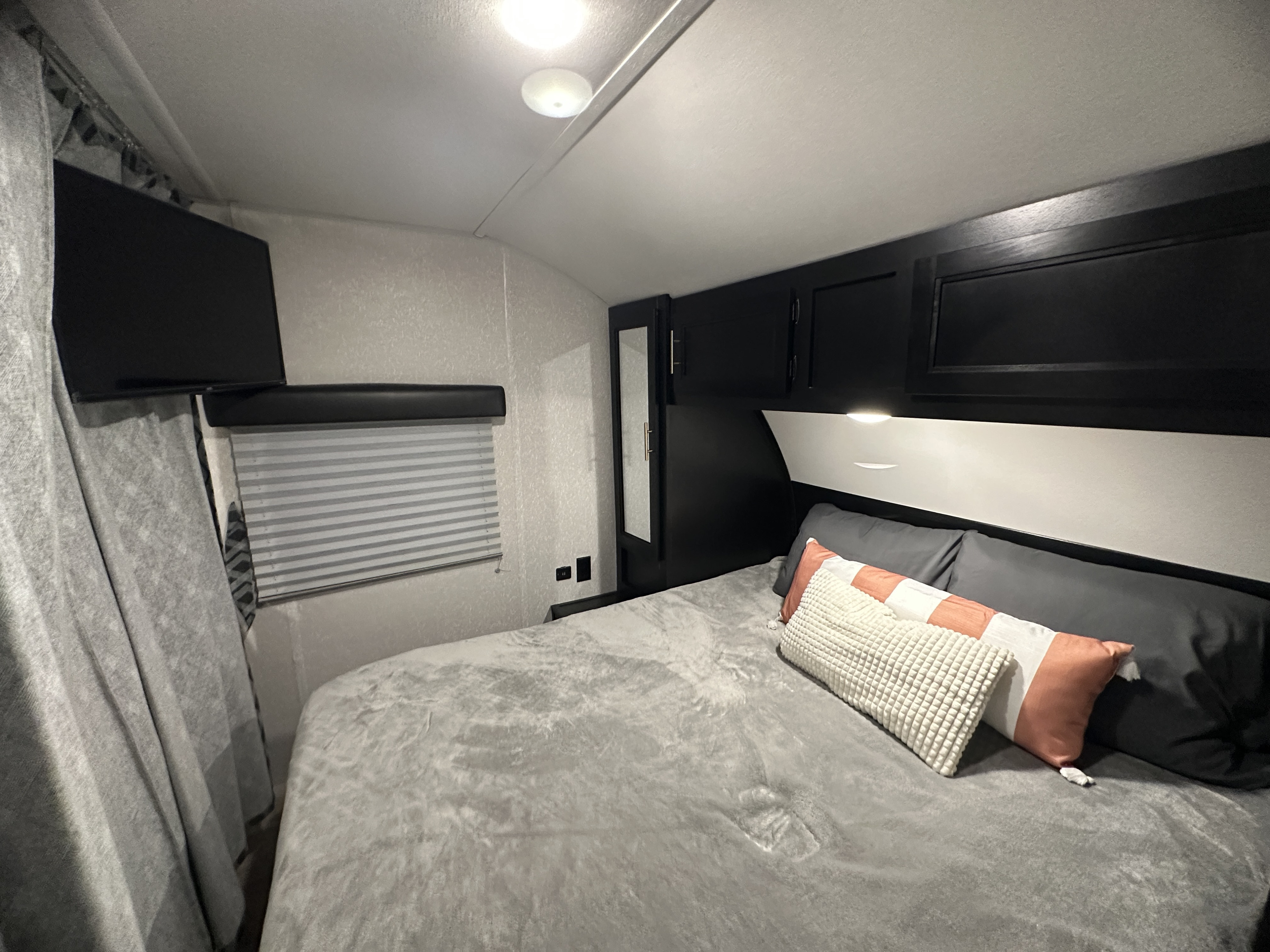 Cozy RV rental bedroom showcasing a comfortable bed, wall-mounted TV, and overhead storage for your journey.. Forest River Cherokee Grey Wolf Special Edition 2022