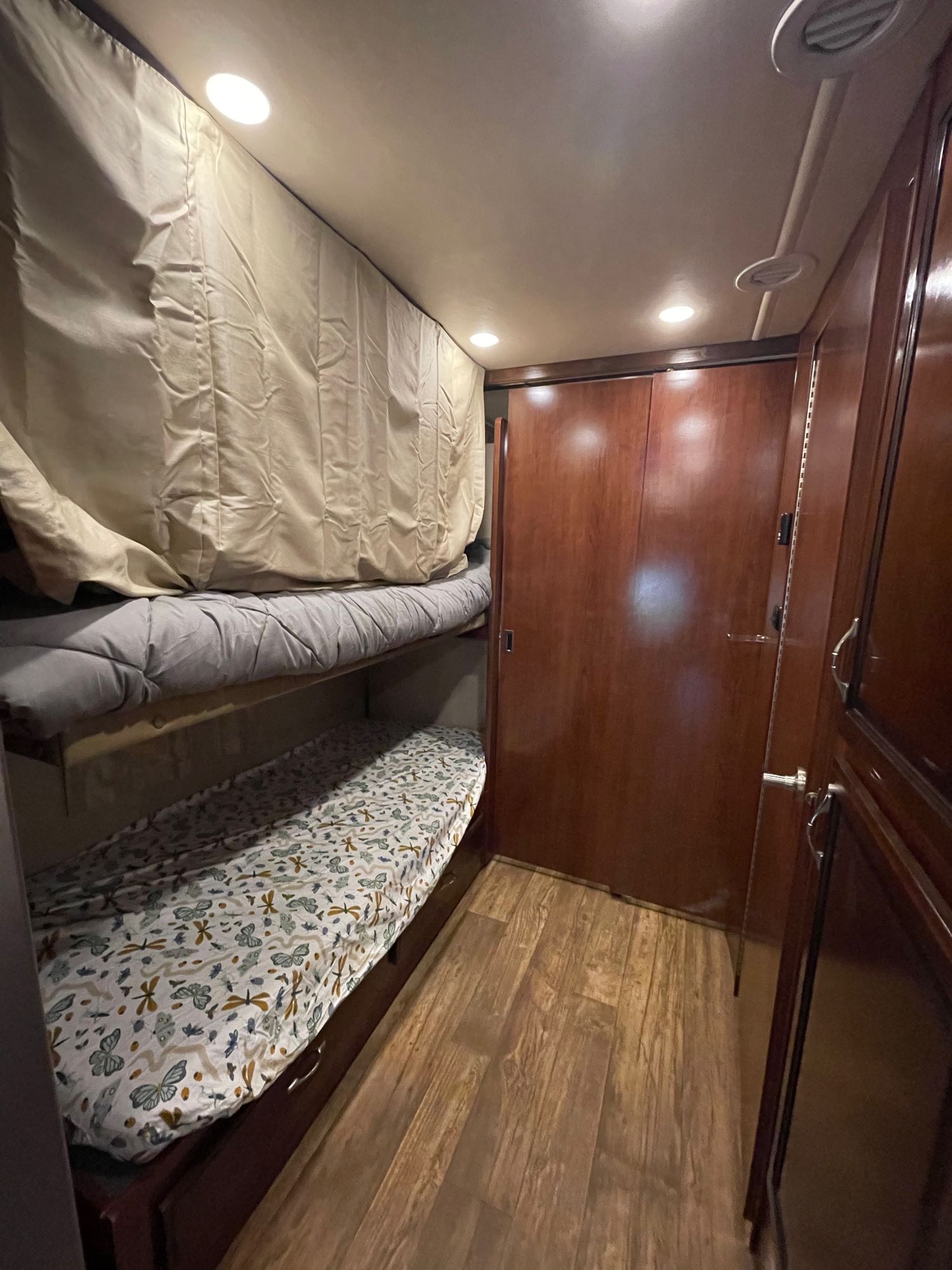 Cozy RV rental interior showcasing bunk beds with patterned sheets, wood cabinets, and ceiling lights, ideal for travel.. Jamboree Jamboree Motorhome 2017