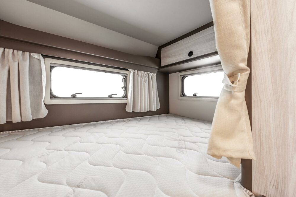 Experience comfort in this clean RV rental interior featuring a spacious sleeping area with a comfortable mattress, windows, and overhead storage. Ideal for travel.. Rimor Kilig 18 2023