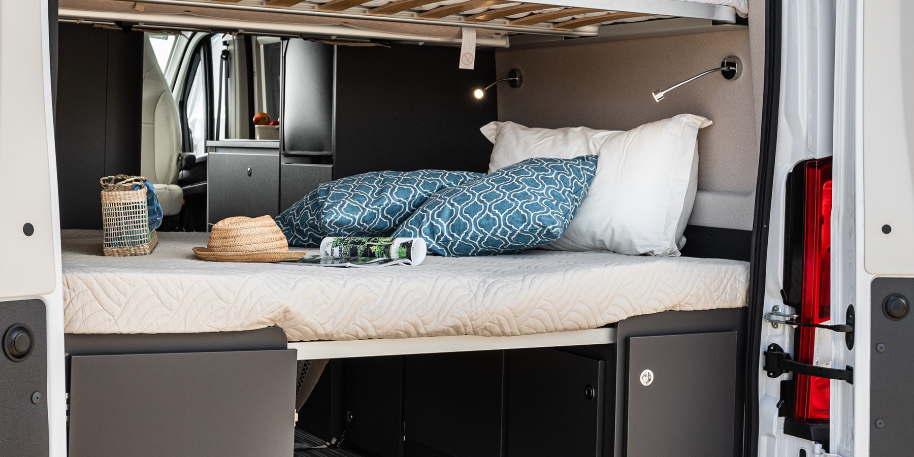 Inside an RV rental, a comfy bed with pillows & reading lights, storage below, & an open rear door for travel.. Fiat MC LOUIS MENFYS 3 MAXI S-LINE 2023