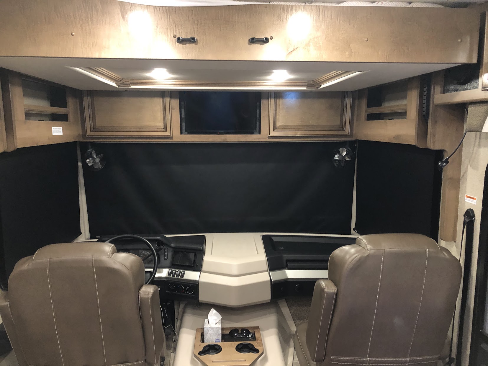 Interior of an RV rental: driver's and passenger's area with brown leather seats, dashboard, privacy shades, and overhead TV.. Fleetwood Bounder 35K 2020