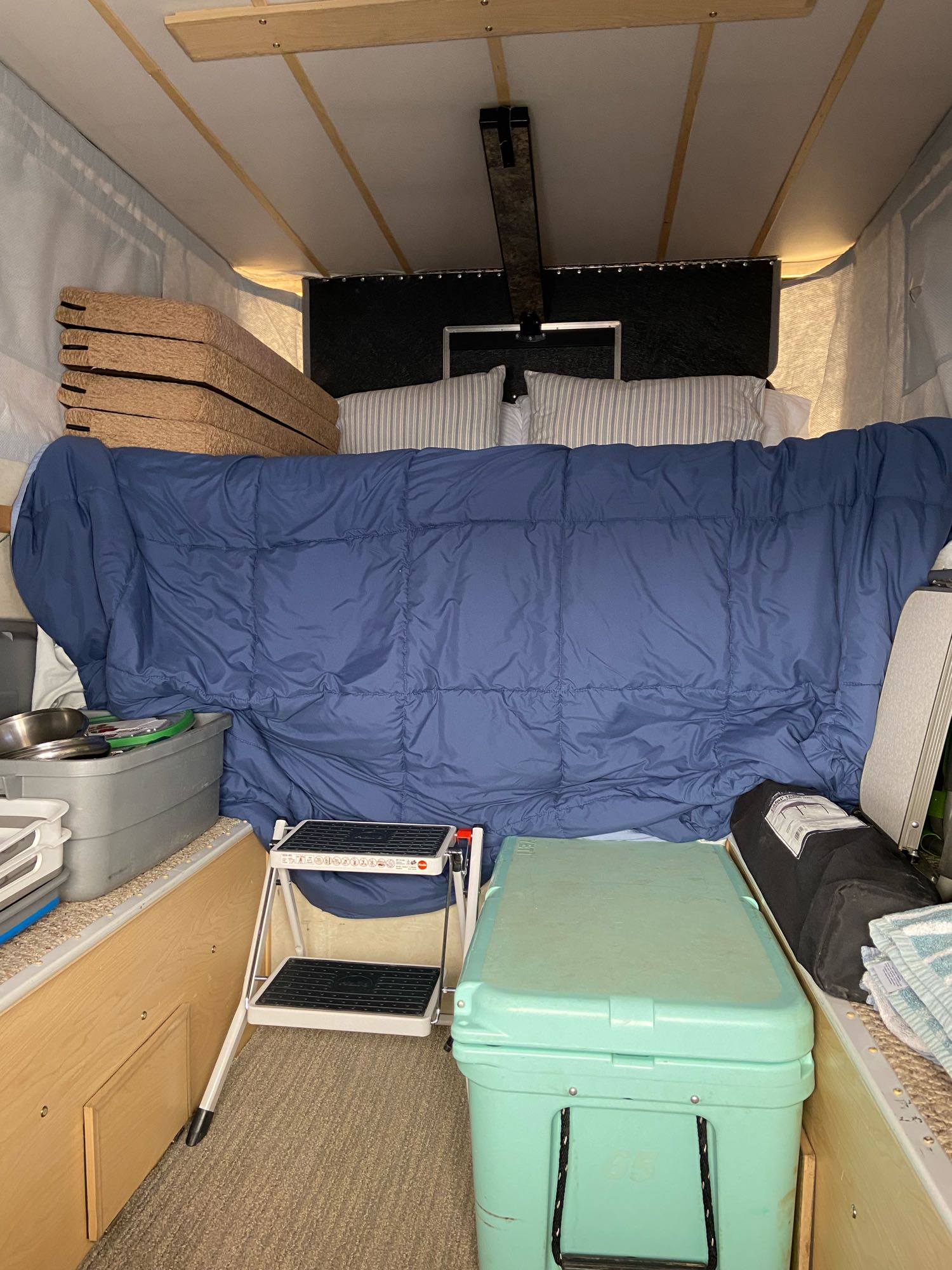 Bed, stacked cushions, cooler, and step stool in this neat RV rental pop-up camper interior.. Four Wheel Campers Shell Models 2014