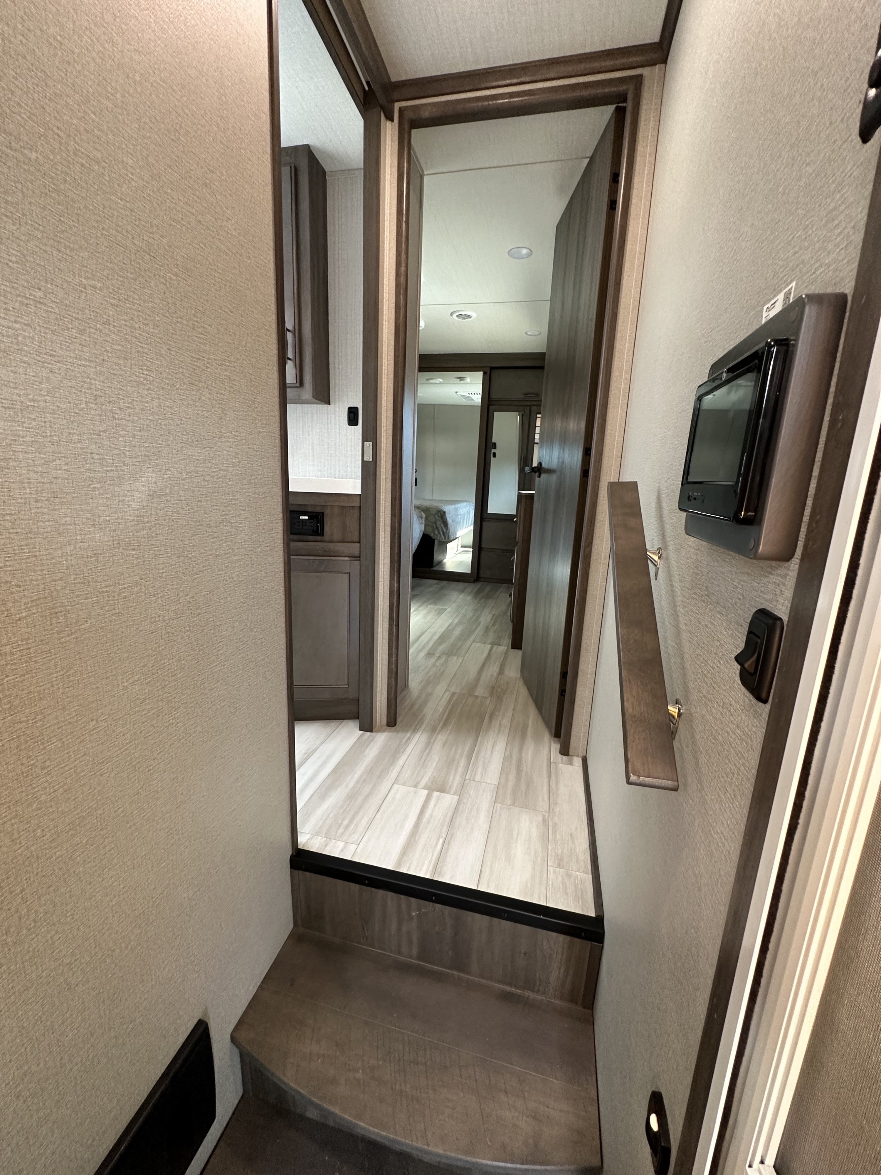 RV rental interior: Steps lead to a modern hallway with a control panel and handrail, looking into a bedroom.. Grand Design Solitude S-Class 2023