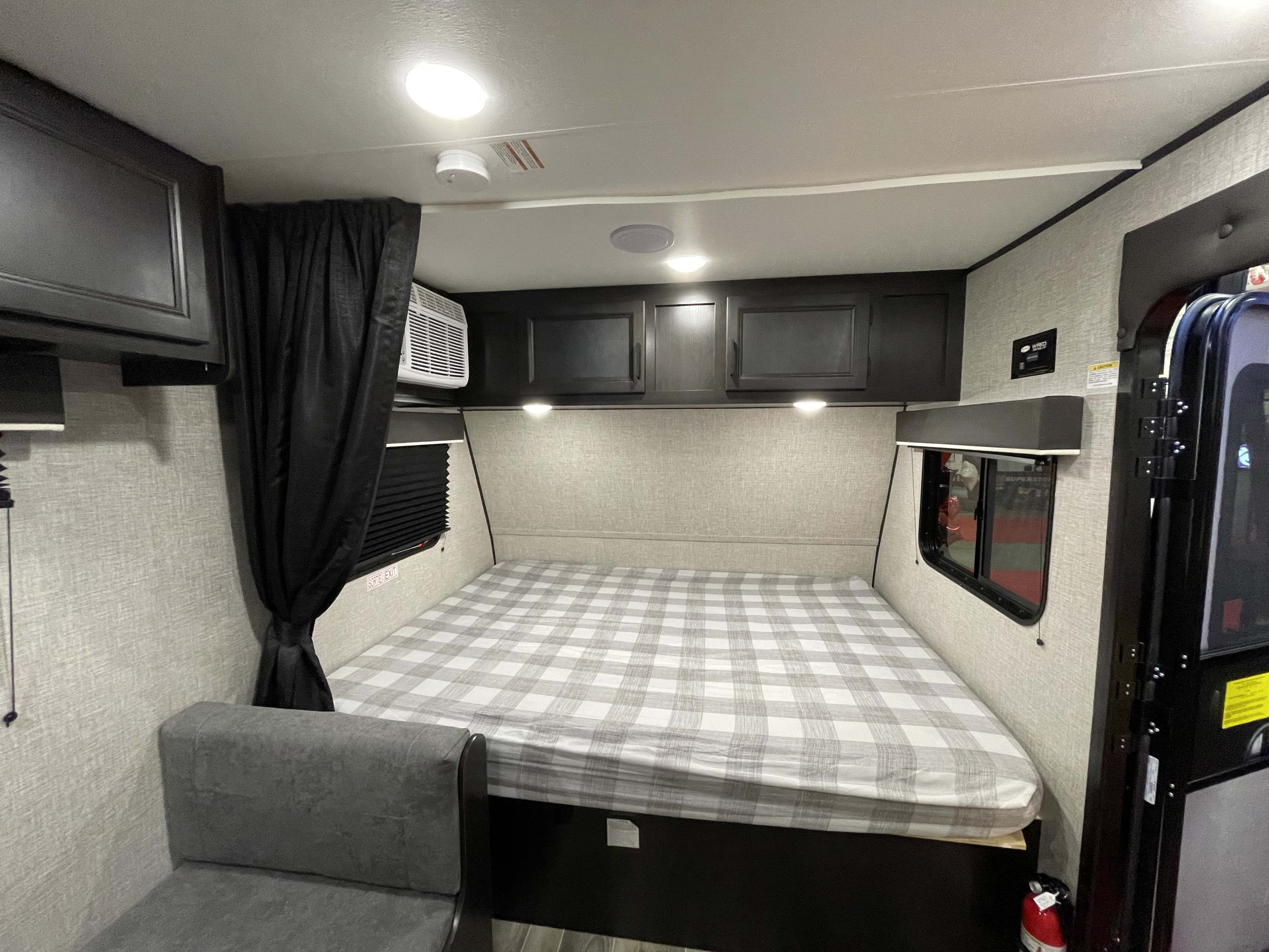 Inside an RV rental: a comfortable bed with plaid bedding, overhead cabinets, an AC unit, and a small sofa.. Jayco Jay Flight SLX 2022