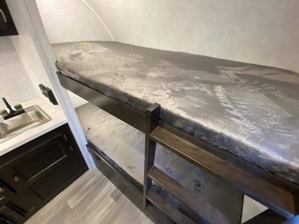 Cozy RV rental interior with bunk beds & compact kitchen counter featuring a sink. Perfect for travel adventures.. Braxton Creek Bushwhacker Plus 2021