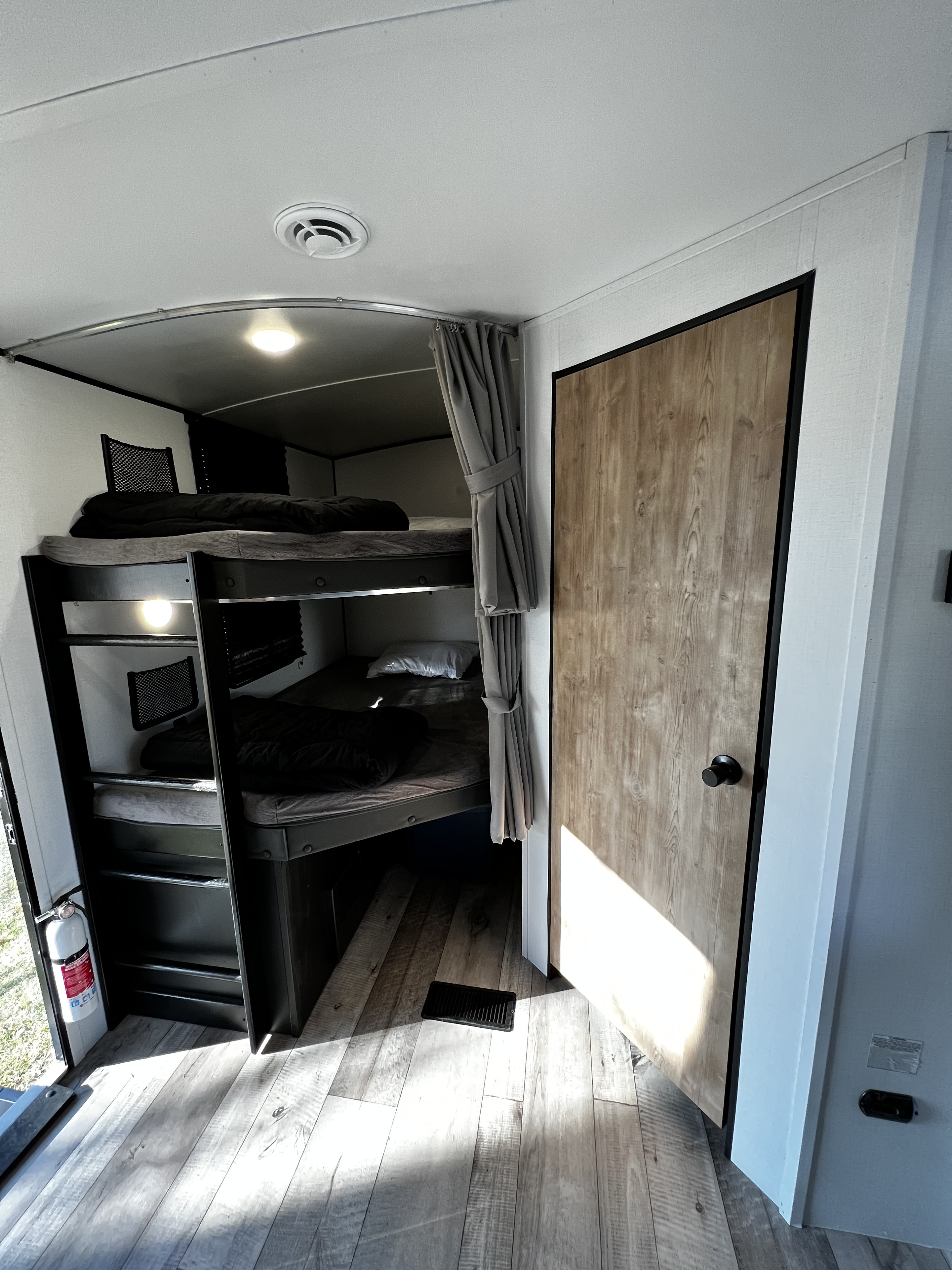 RV rental bunkhouse featuring three beds, wood-look flooring, and a fire extinguisher. Bright, modern, and ready for adventure.. Keystone RV Springdale 2022